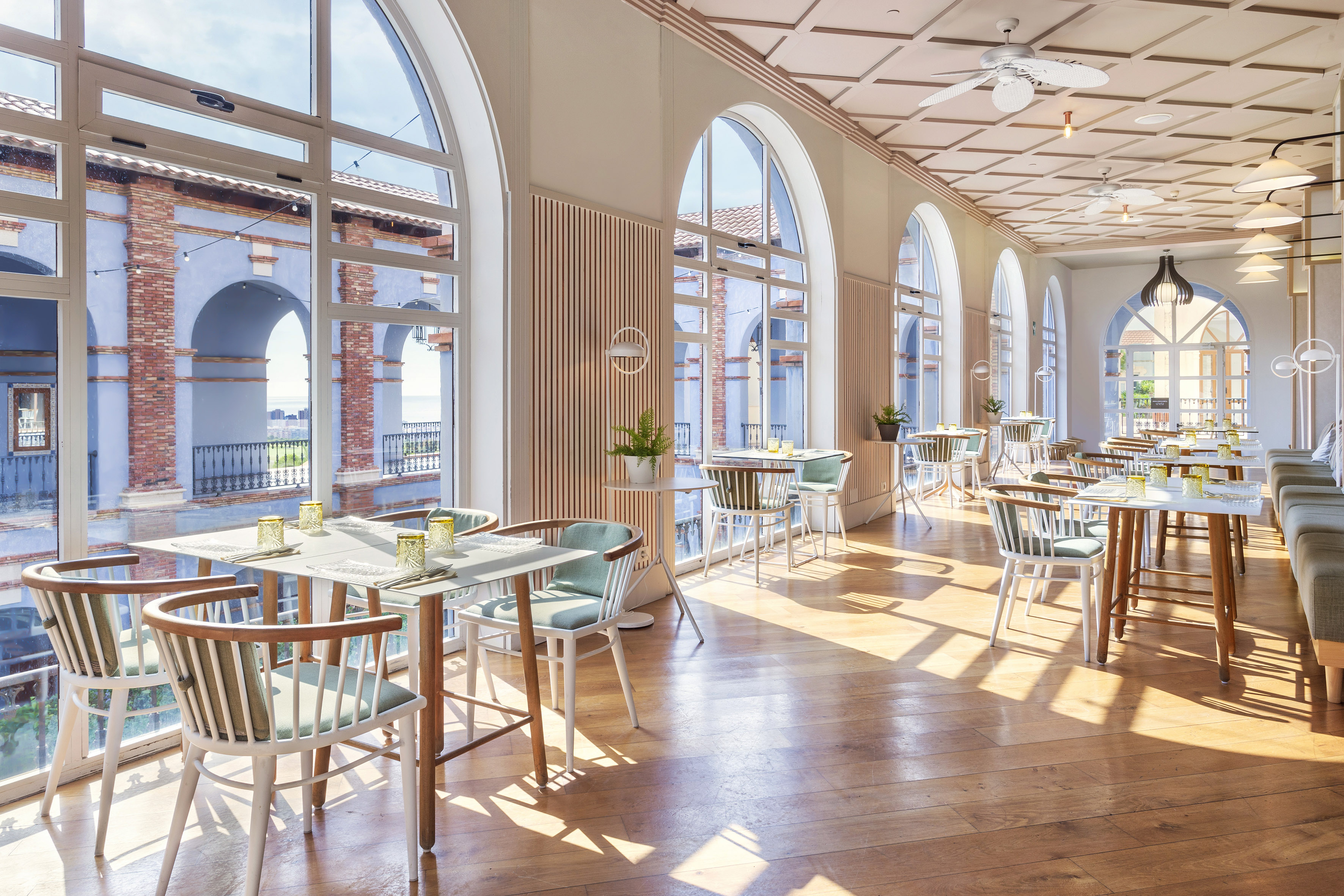 Modern coastal restaurant with arched windows, wooden floors, set tables.