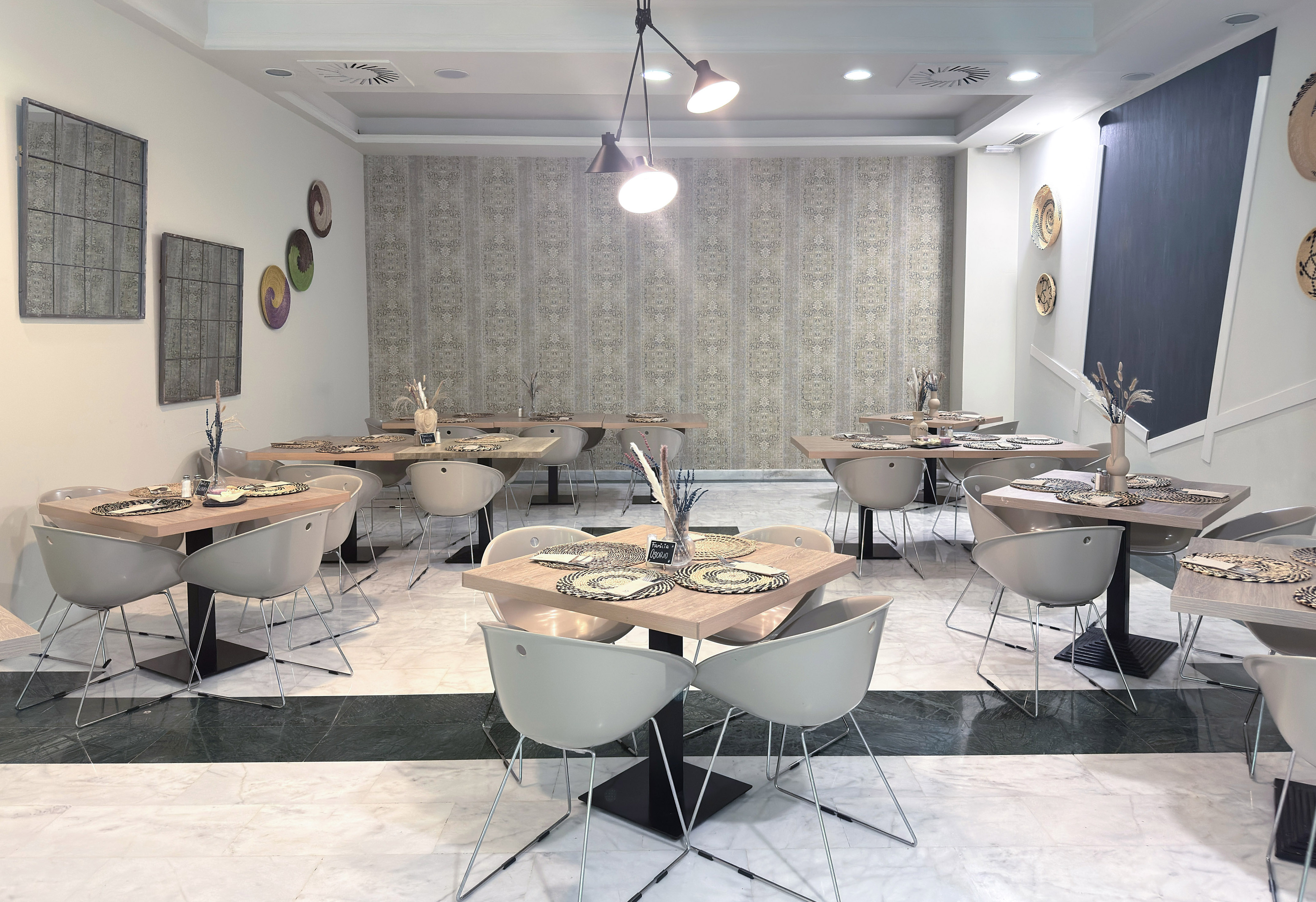 Modern restaurant dining room with wooden tables, grey chairs, and patterned wall.