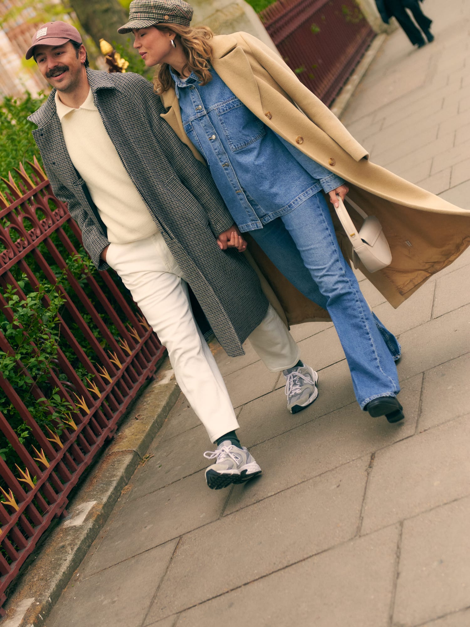 Fashionable couple in fall coats and denim walking hand-in-hand on a city street.