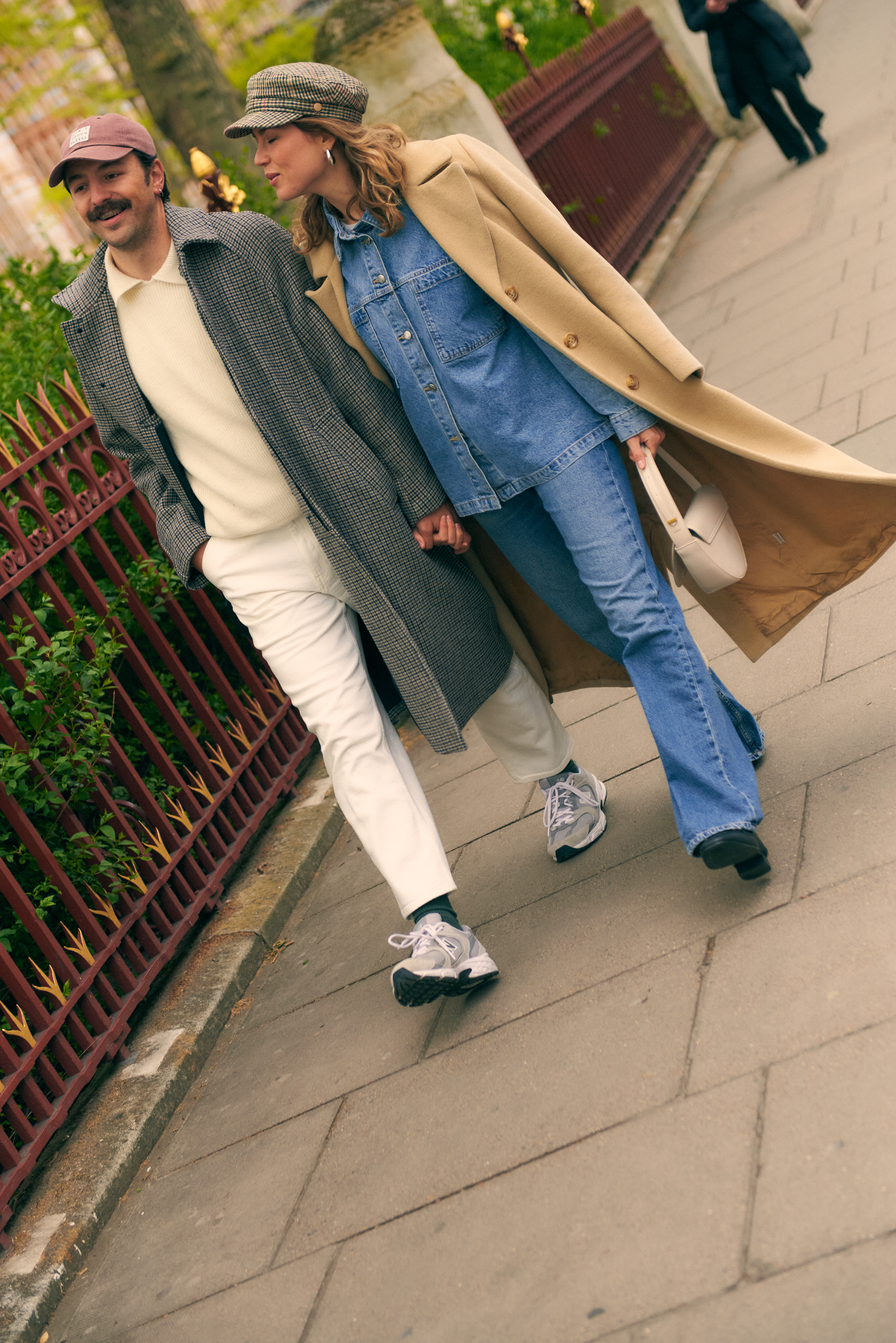 Fashionable couple in fall coats and denim walking hand-in-hand on a city street.
