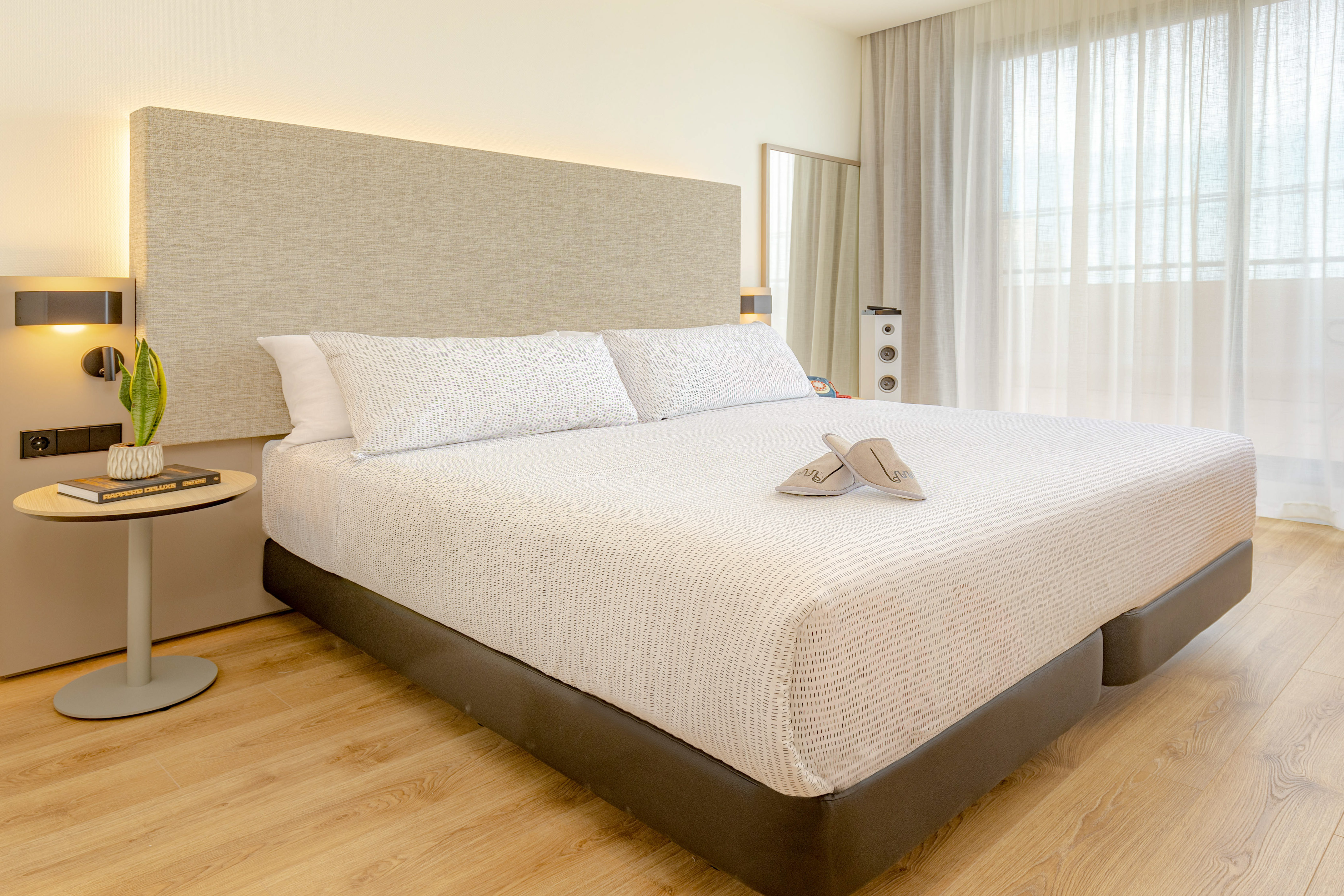 Modern hotel bedroom with white bed, neutral headboard, and wood floor.