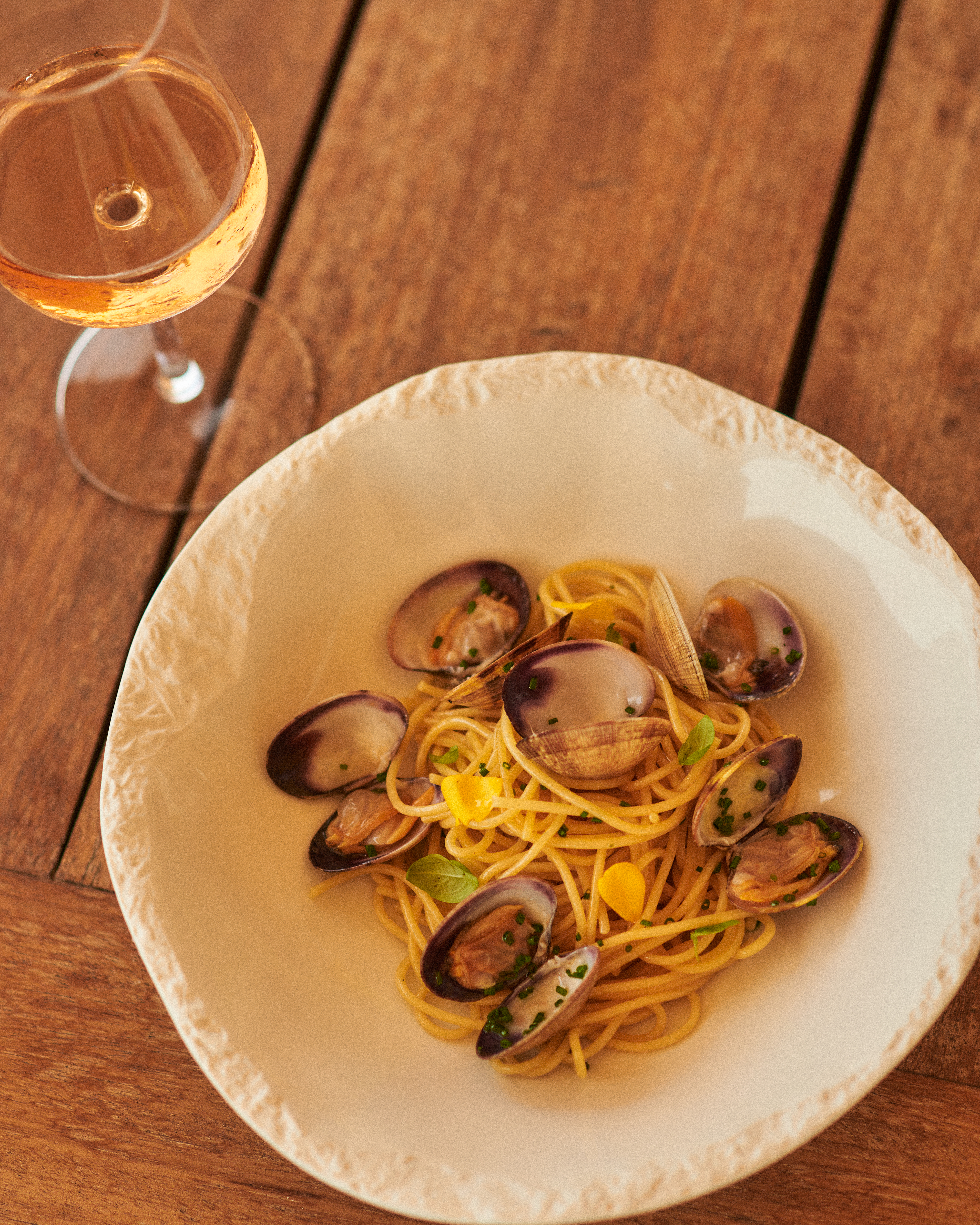 Spaghetti alle vongole, garnished with herbs, beside a glass of rose wine.