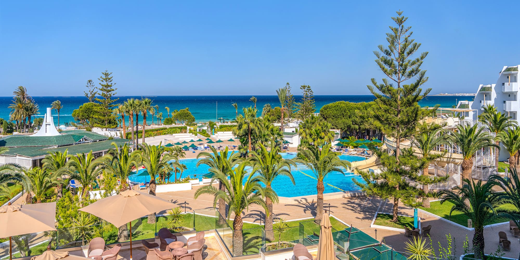 Tropical resort with swimming pools, palm trees, beach, and ocean view.