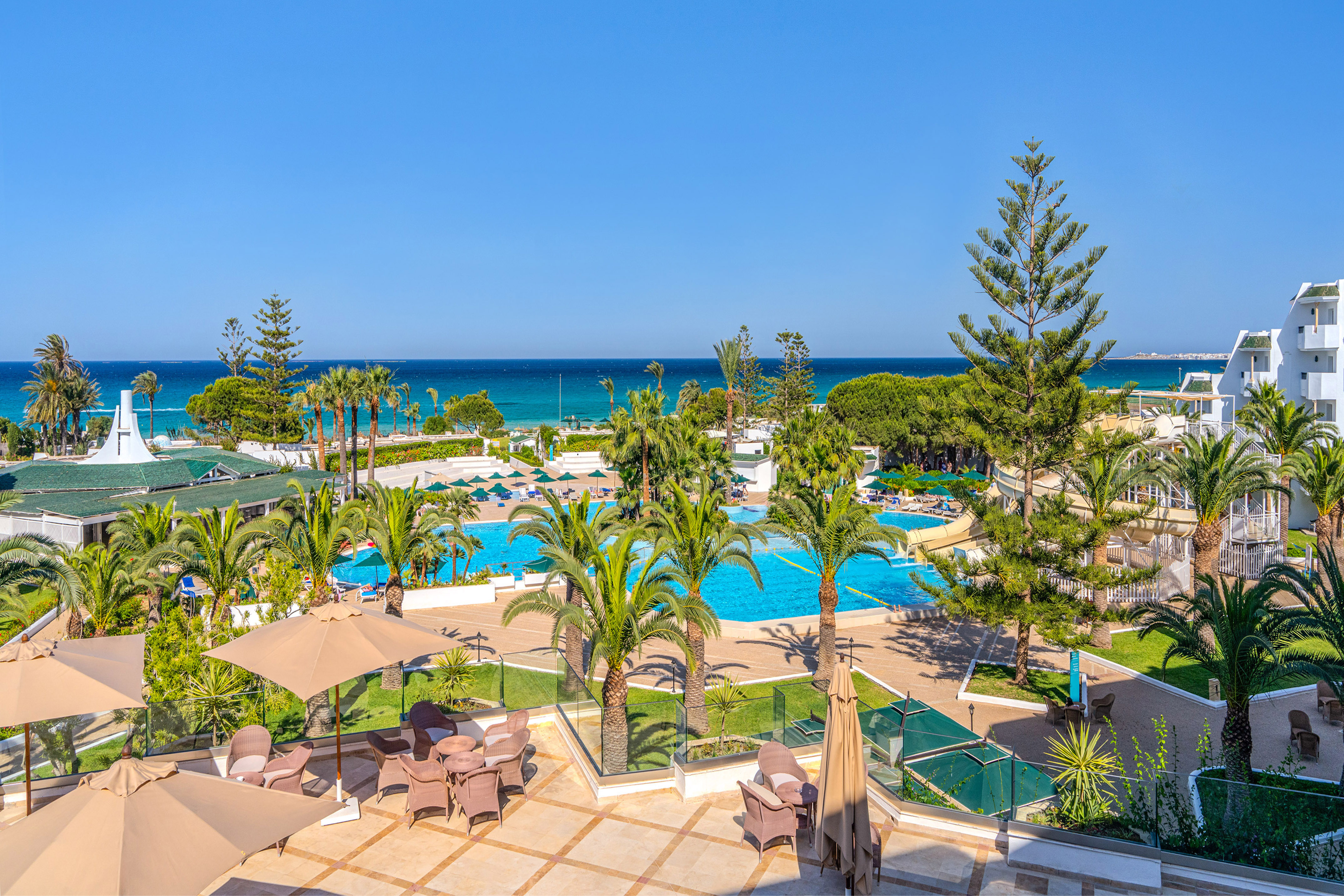 Resort with oceanfront view, swimming pools, palm trees, and sunny terrace.