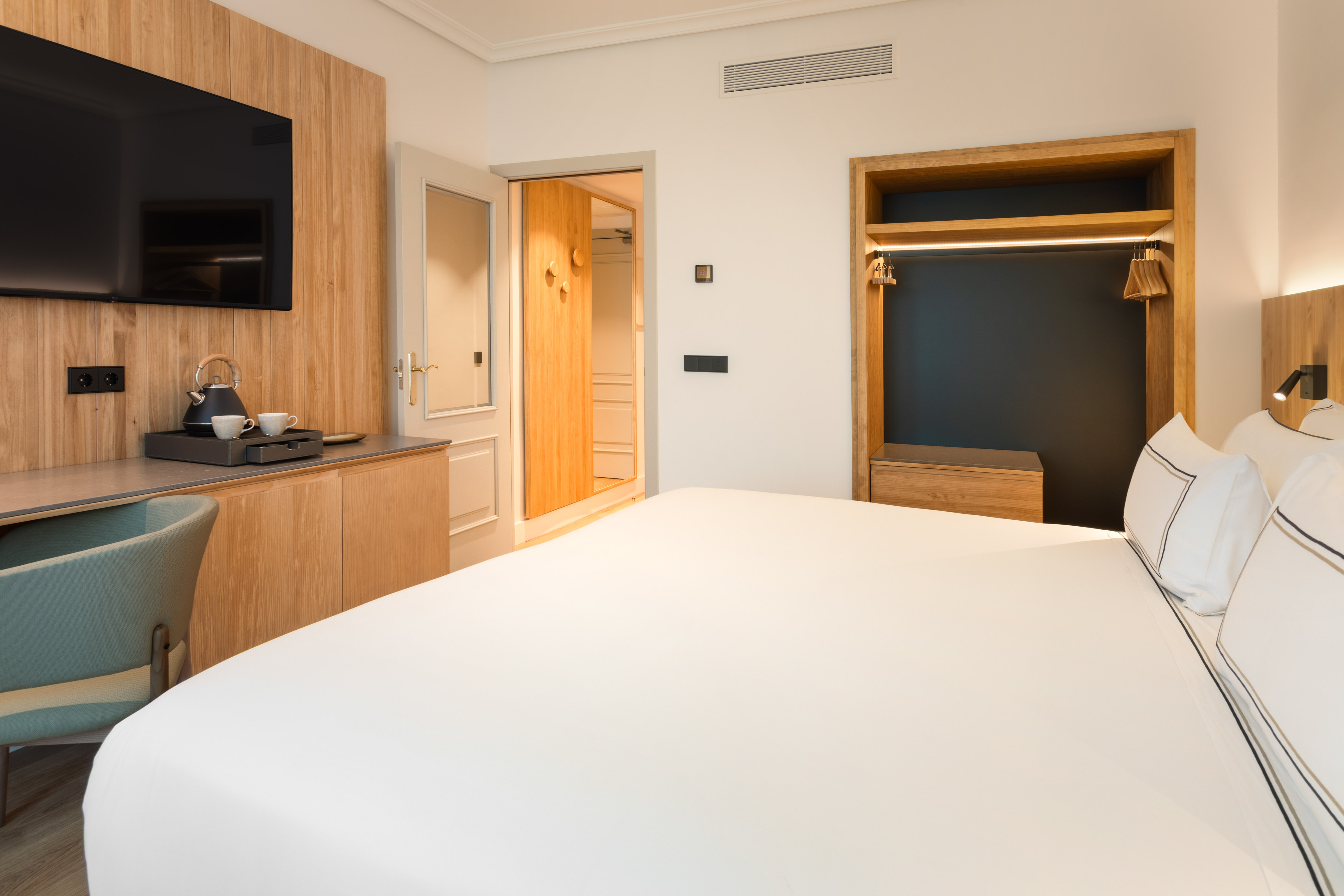 Modern hotel bedroom with large bed, TV, wooden desk, and built-in closet.