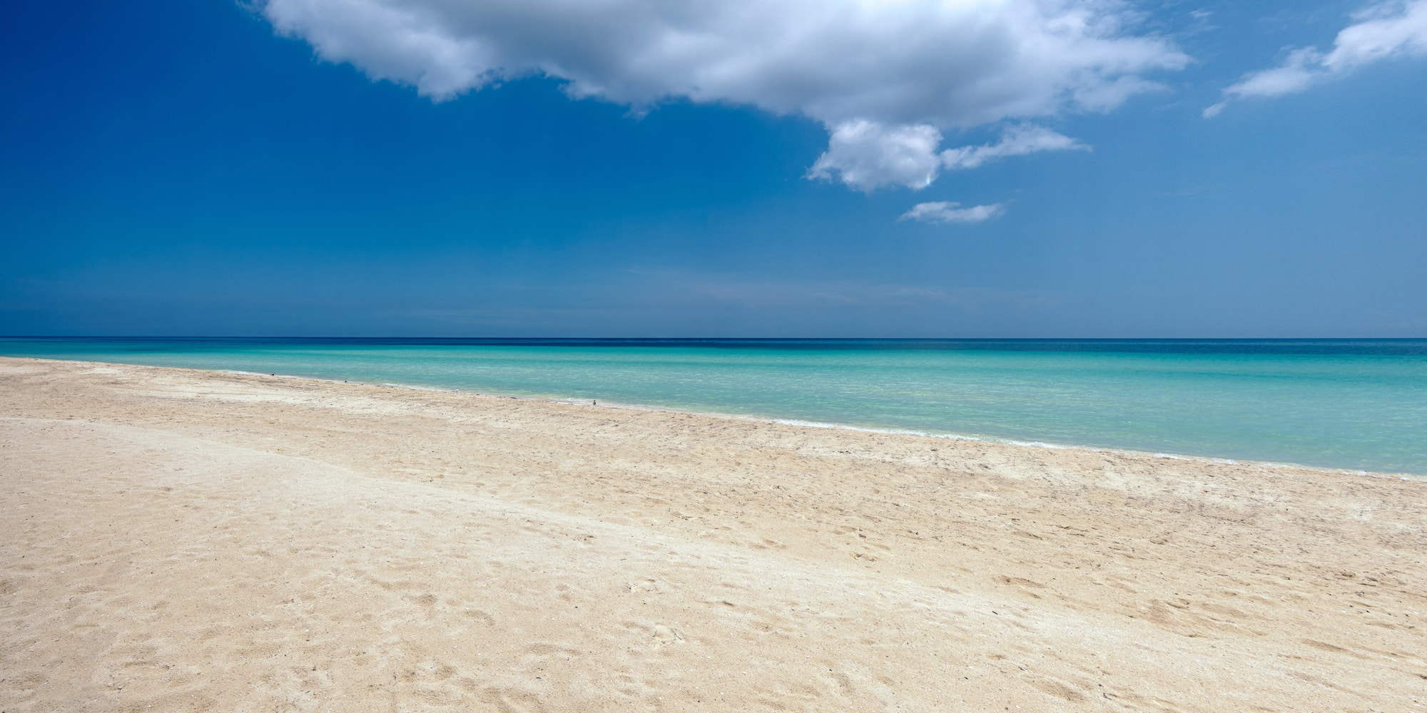 a sandy beach with blue water and clouds