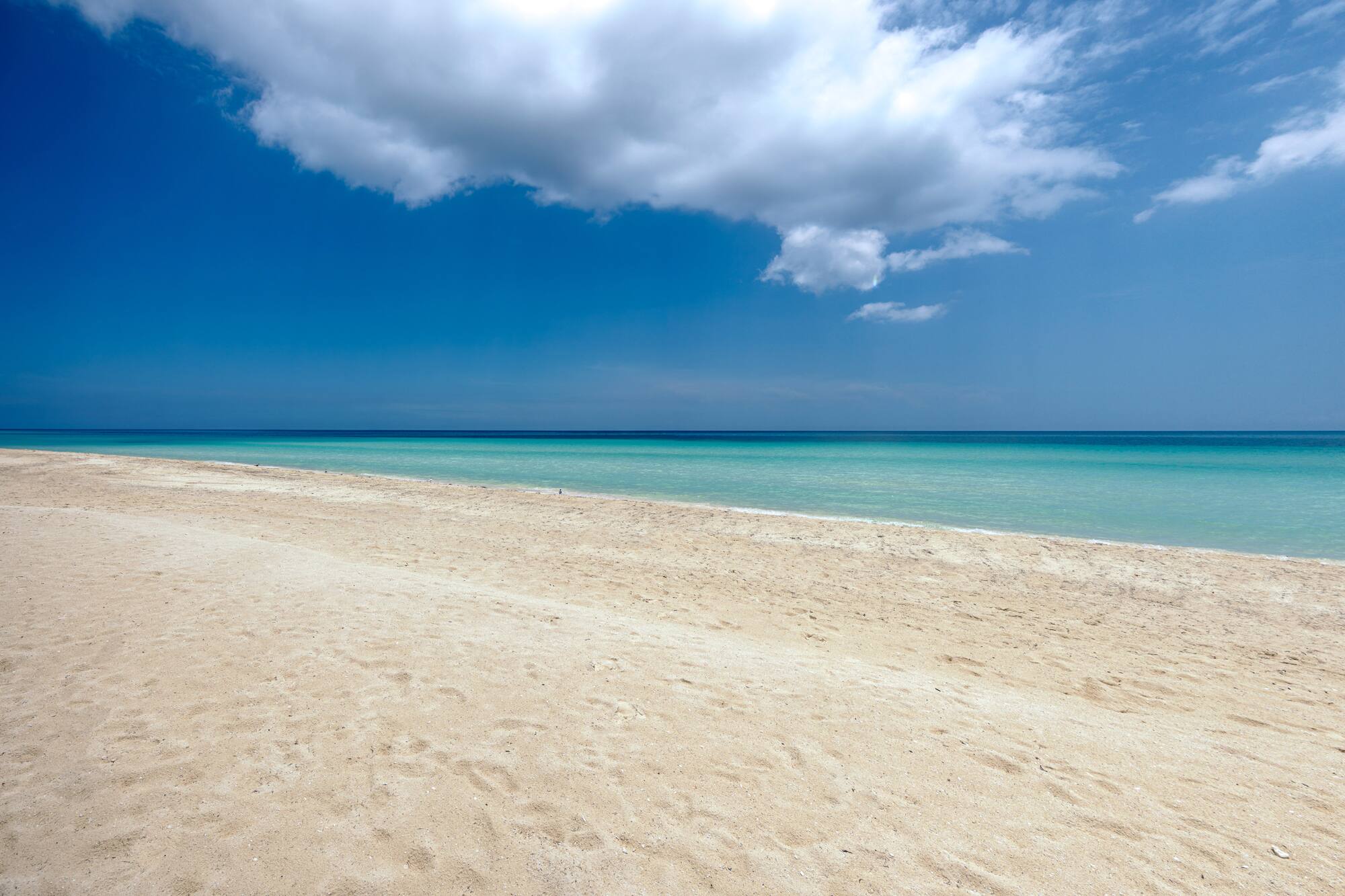 a sandy beach with blue water and clouds