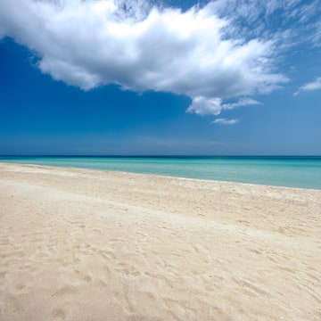 a sandy beach with blue water and clouds