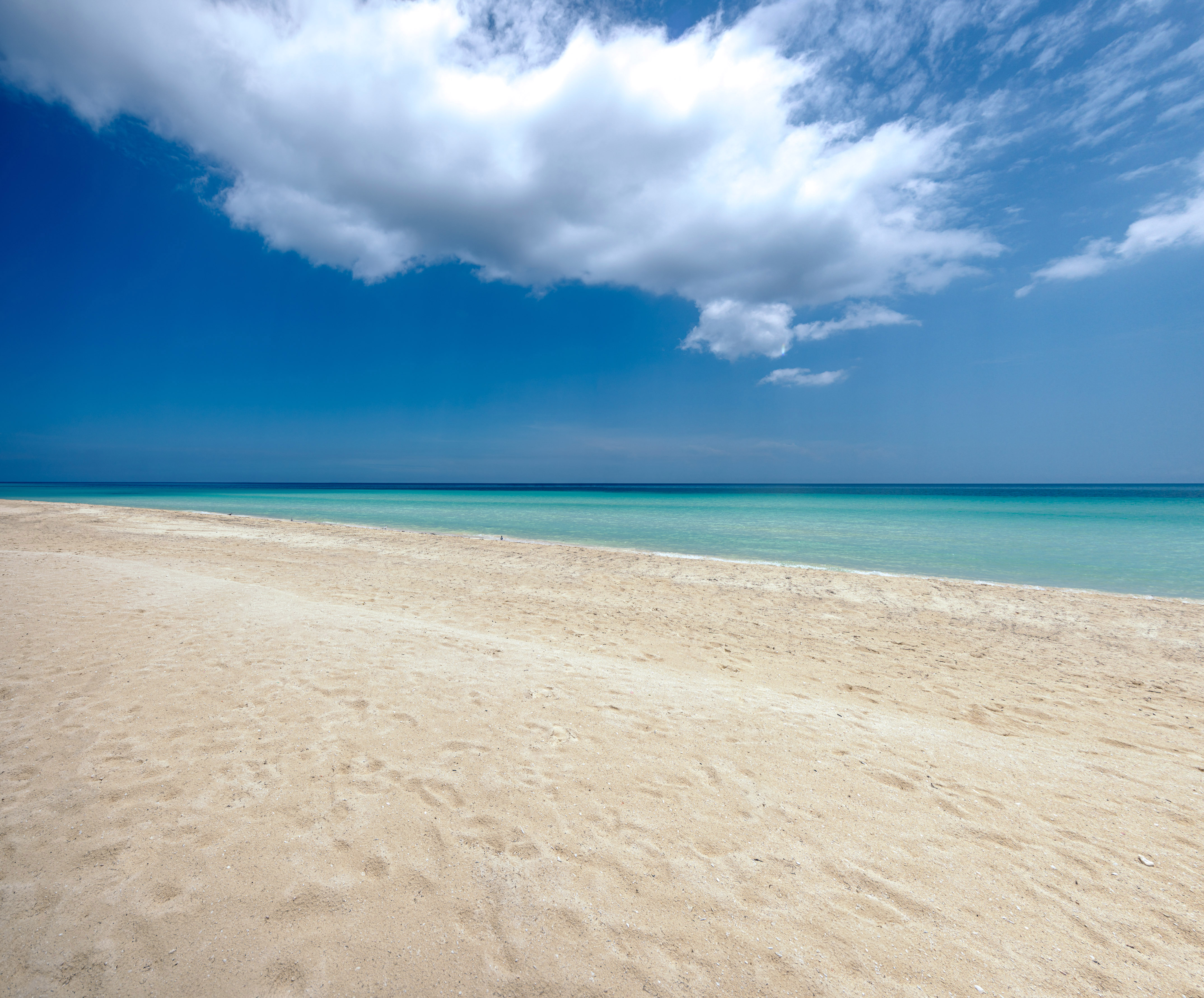 a sandy beach with blue water and clouds