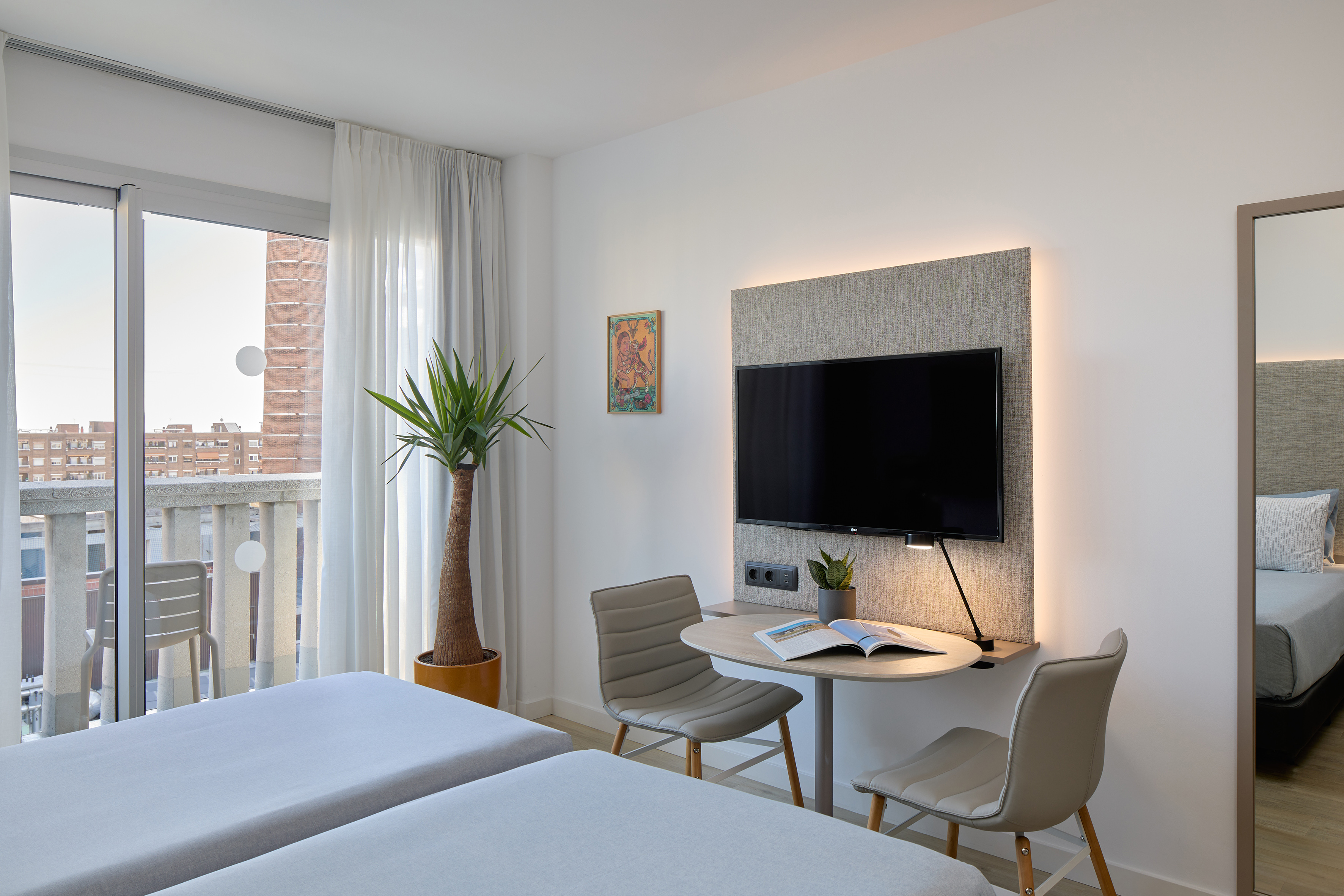 Modern twin hotel room with balcony, city view, TV, and work desk.