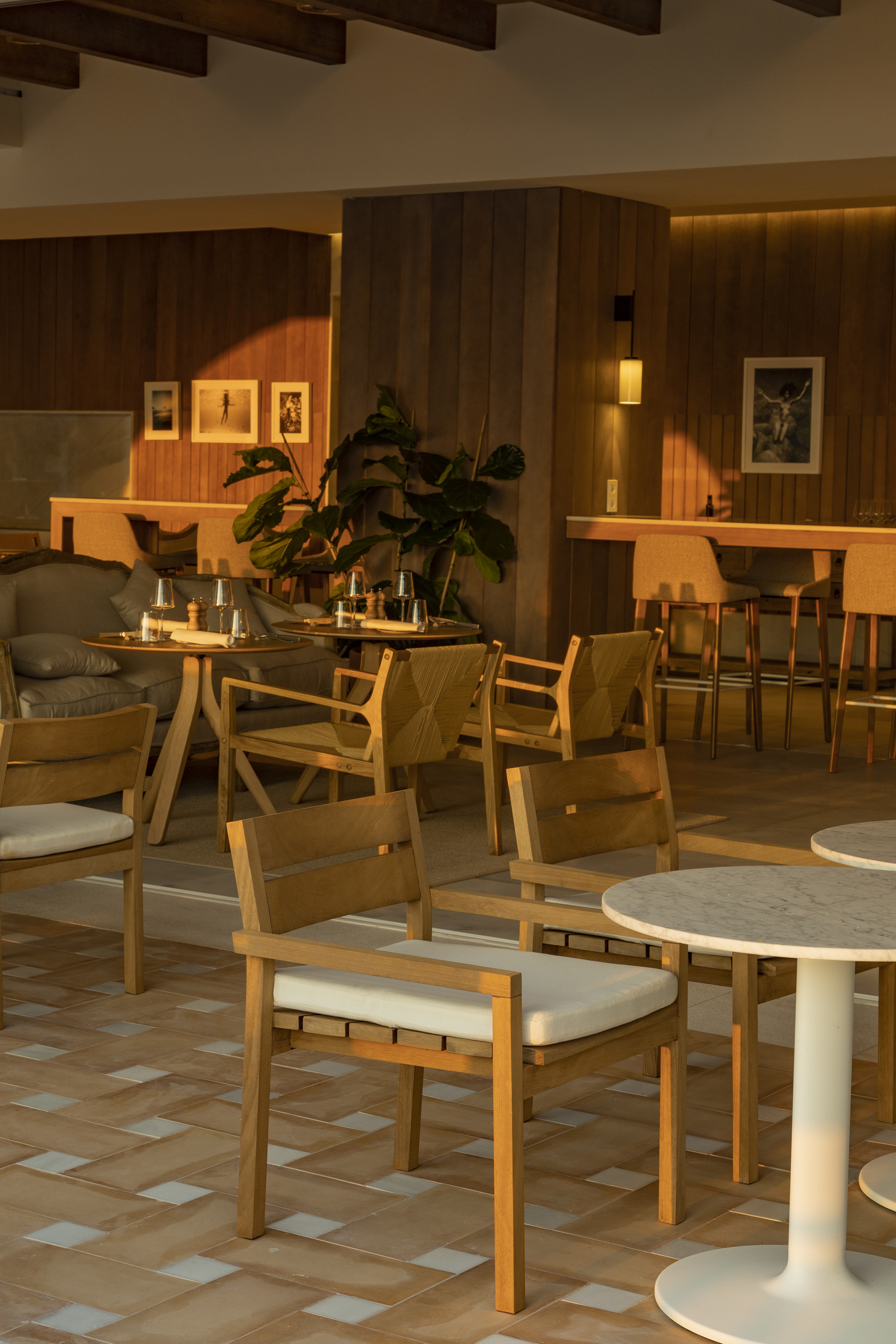 Warmly lit modern restaurant interior with wooden chairs, dining tables, and bar.