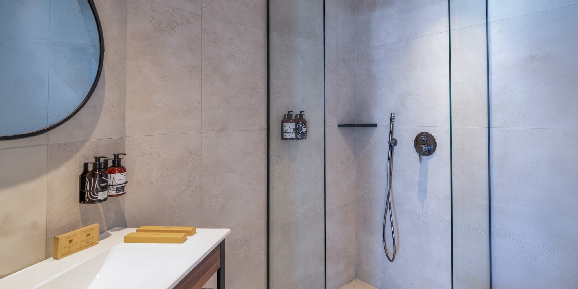 Modern bathroom with walk-in shower, rainfall head, vanity, and round mirror.
