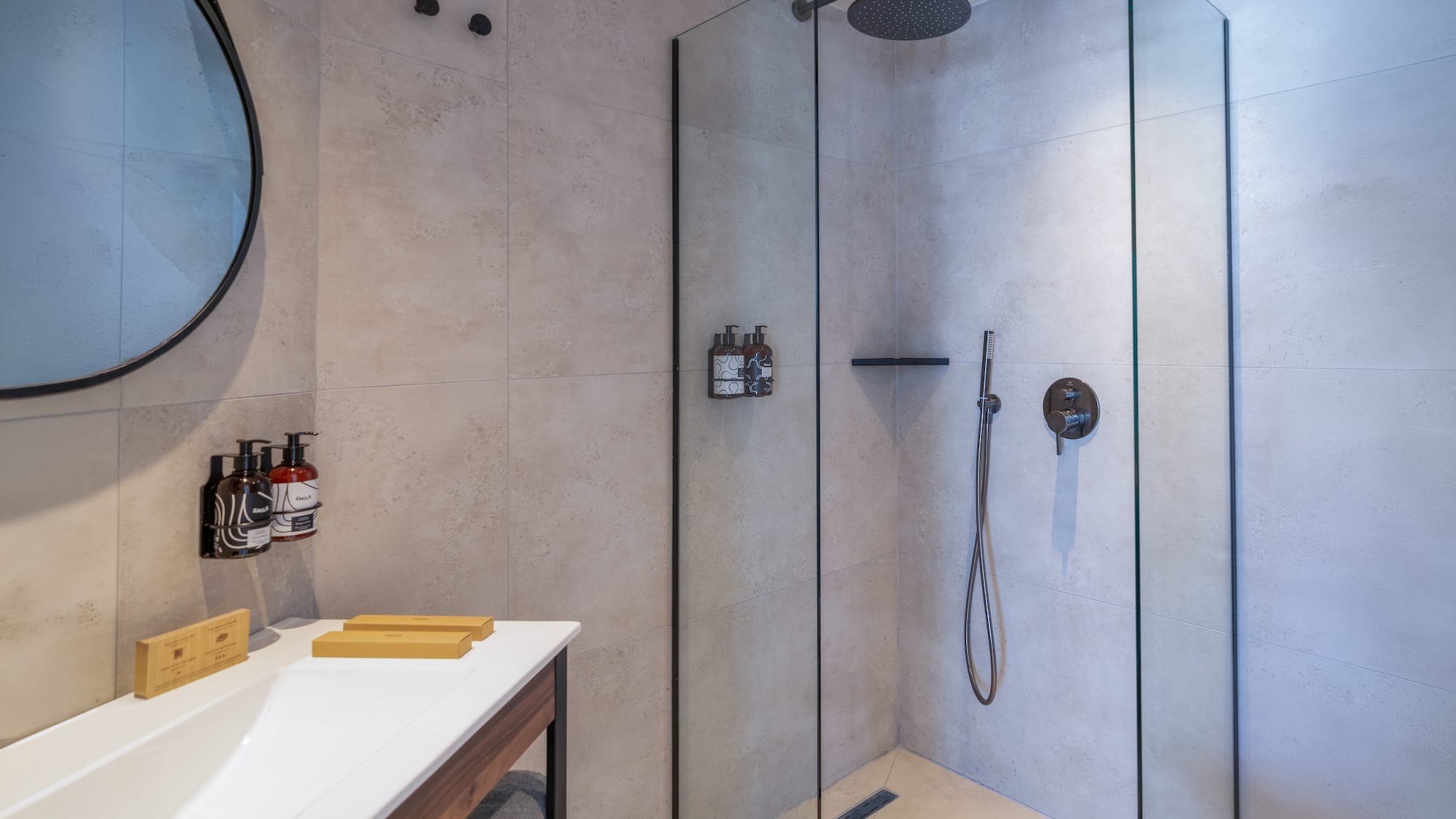 Modern bathroom with walk-in shower, rainfall head, vanity, and round mirror.