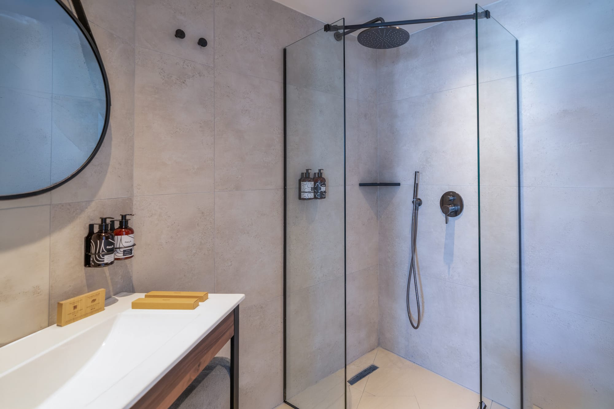 Modern bathroom with walk-in shower, rainfall head, vanity, and round mirror.