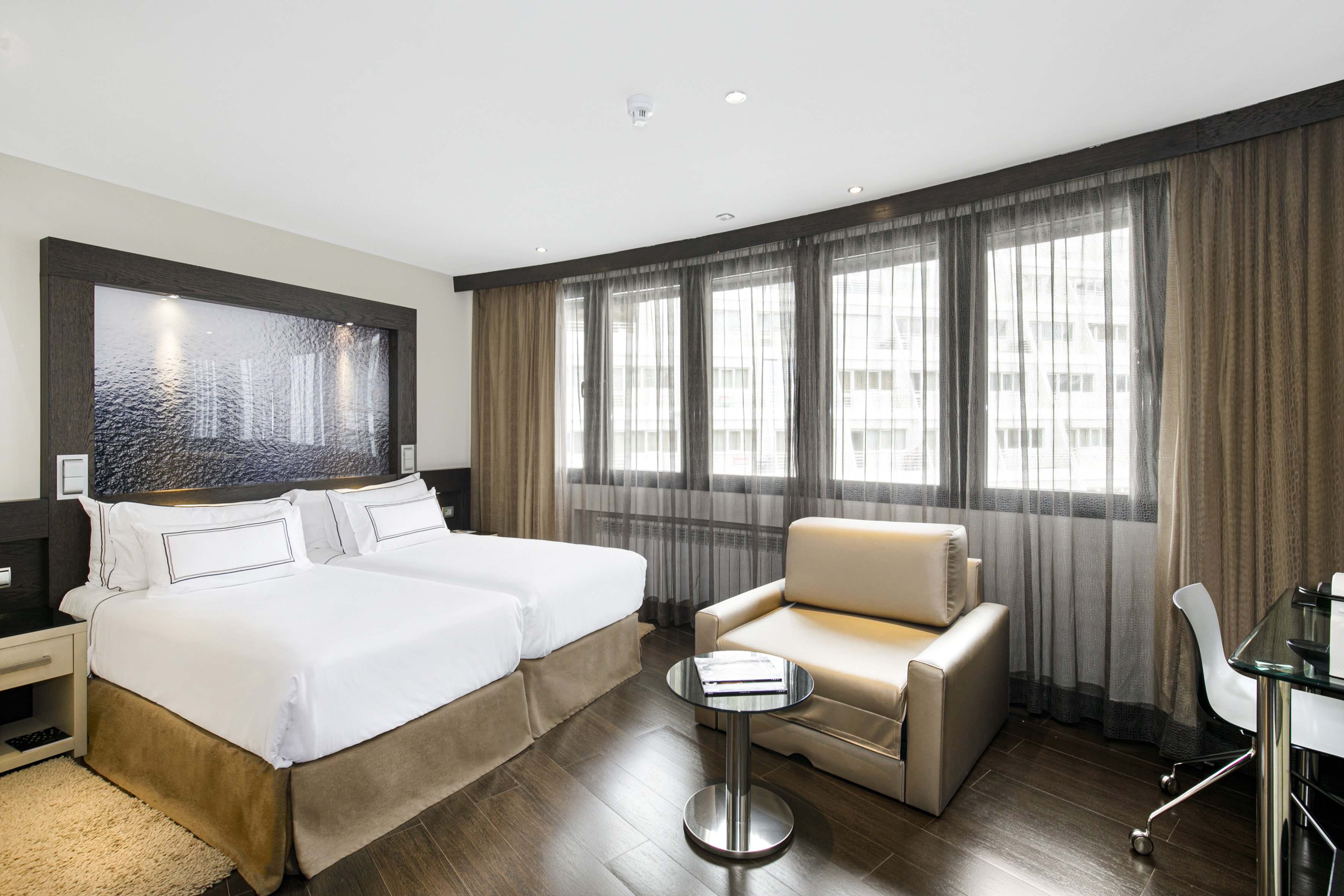 Spacious hotel room with twin beds, sitting area, and dark wood flooring.