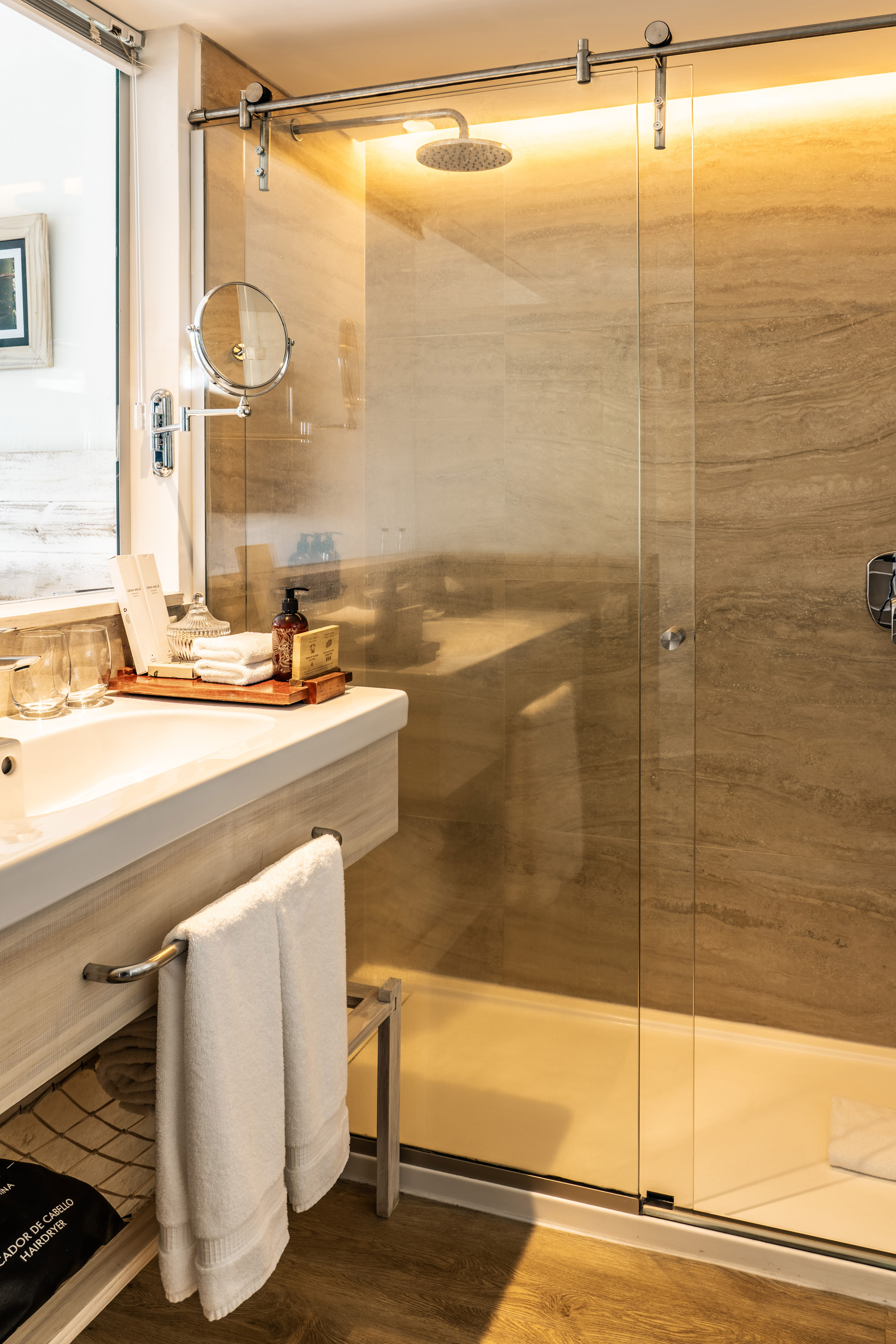Modern hotel bathroom with glass shower, rain showerhead, vanity, and toiletries.