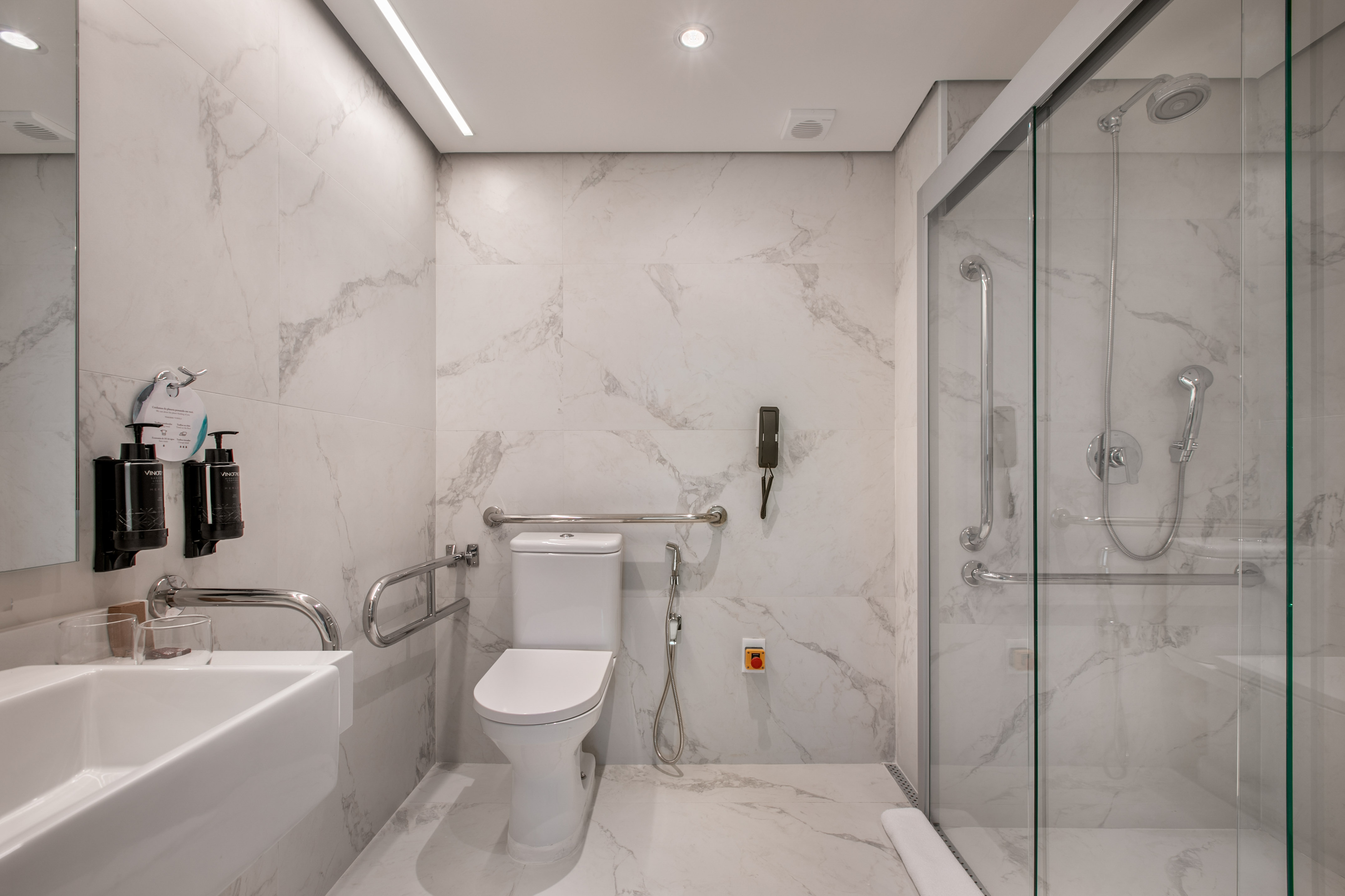Modern accessible bathroom with white marble, toilet, shower, and grab bars.