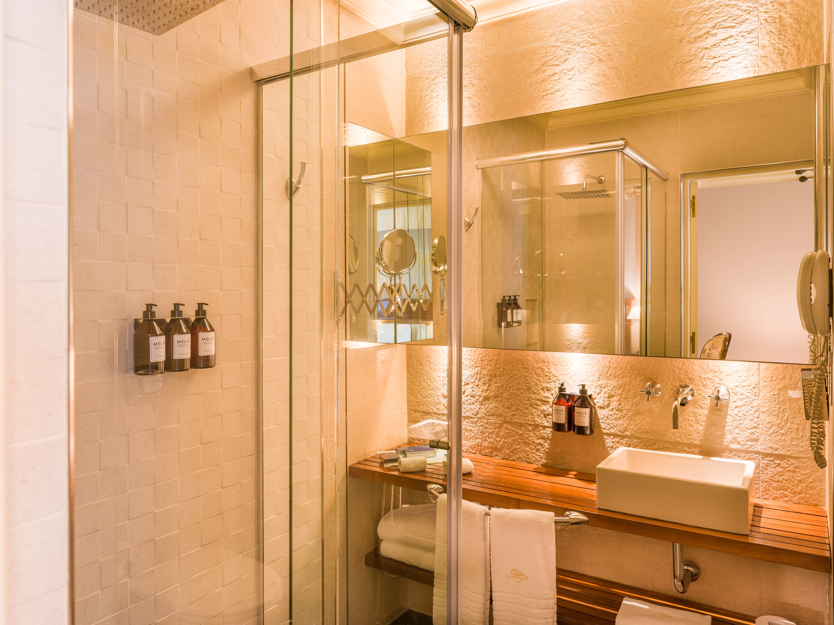 Modern hotel bathroom with glass shower, wood vanity, and white vessel sink.