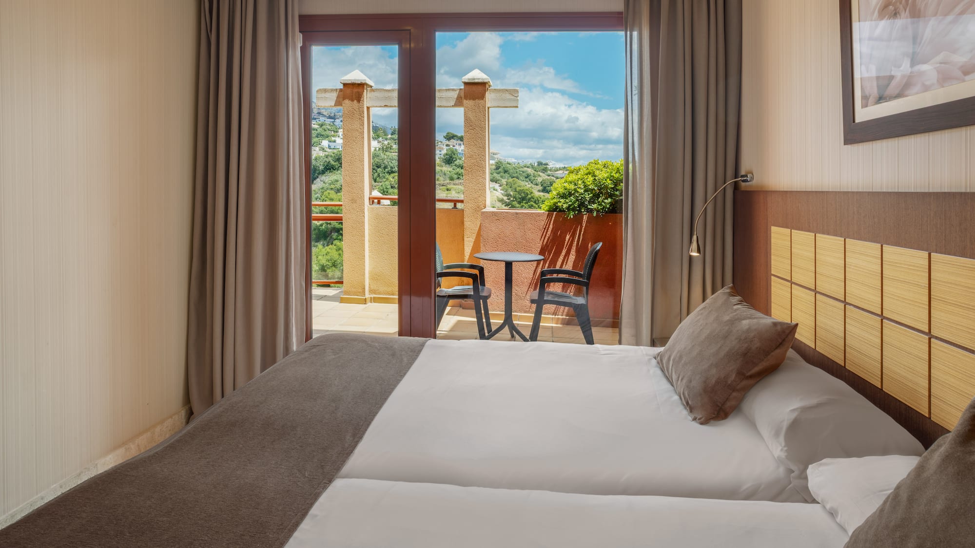 Hotel room with private balcony, outdoor seating, and a scenic hillside view.