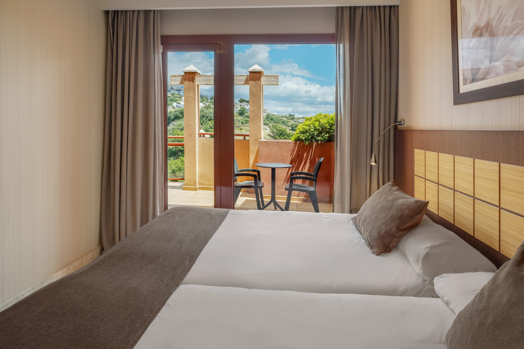 Hotel room with twin beds and balcony overlooking a scenic mountain view.