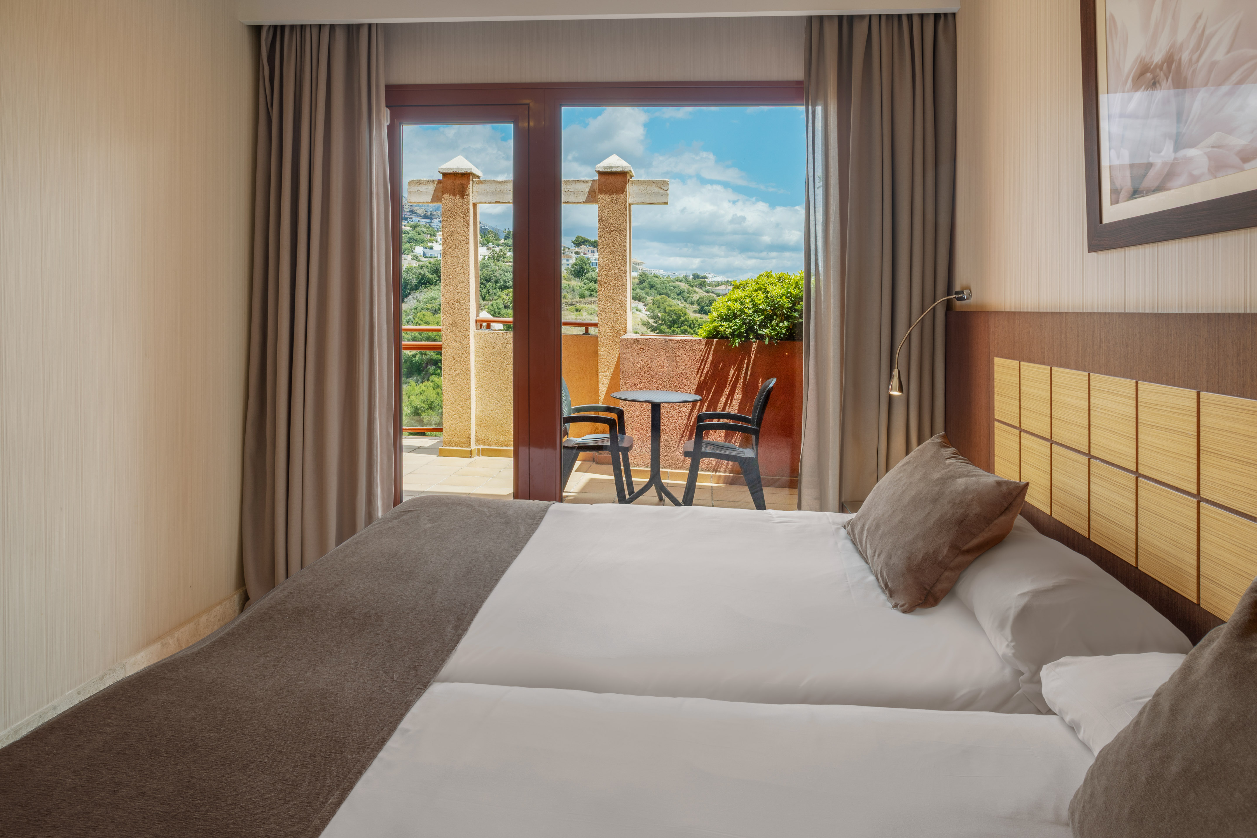 Hotel room with twin beds and balcony overlooking a scenic mountain view.