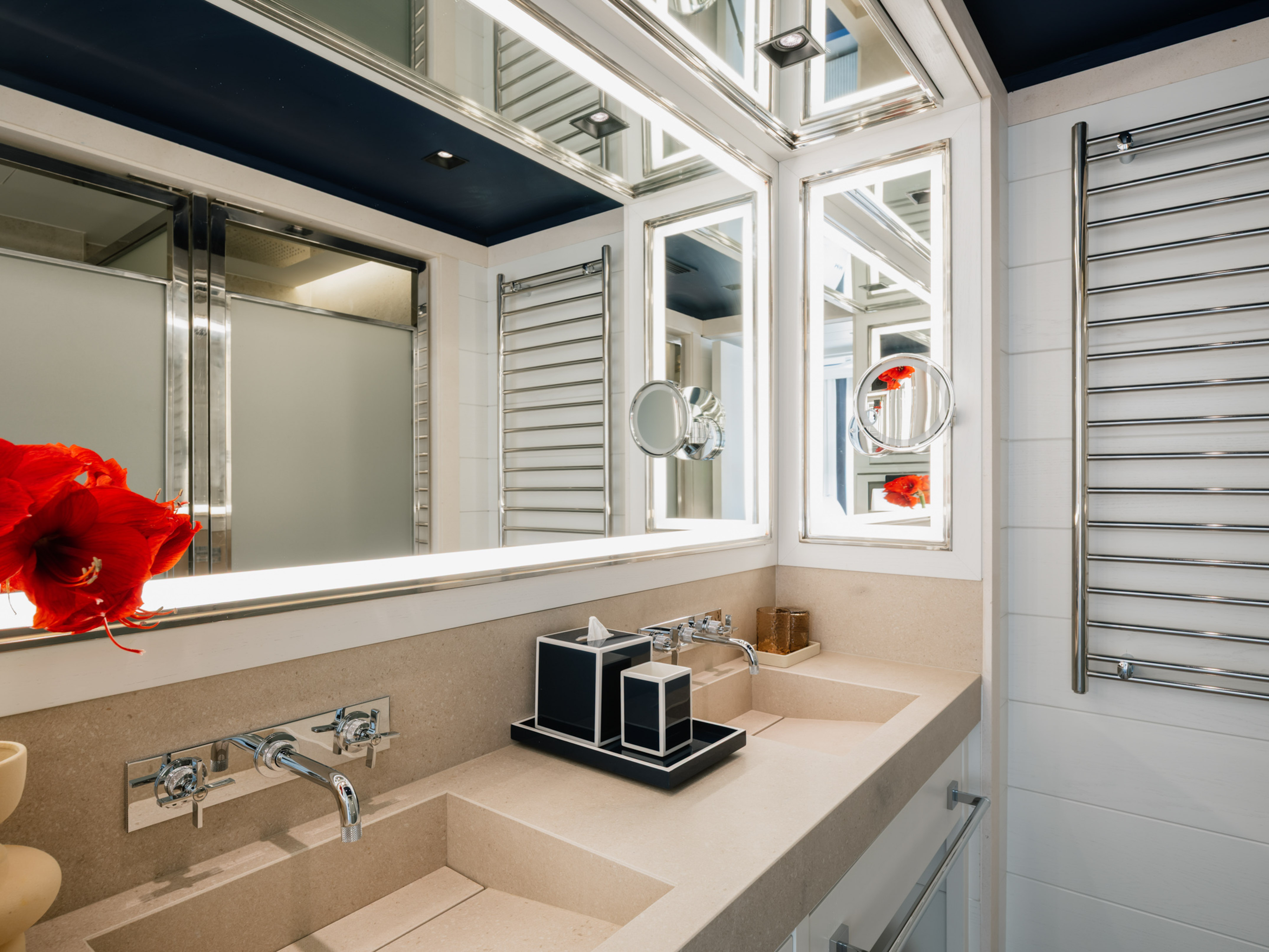 Modern luxury bathroom with dual sinks, lit mirrors, towel warmer, and shower.