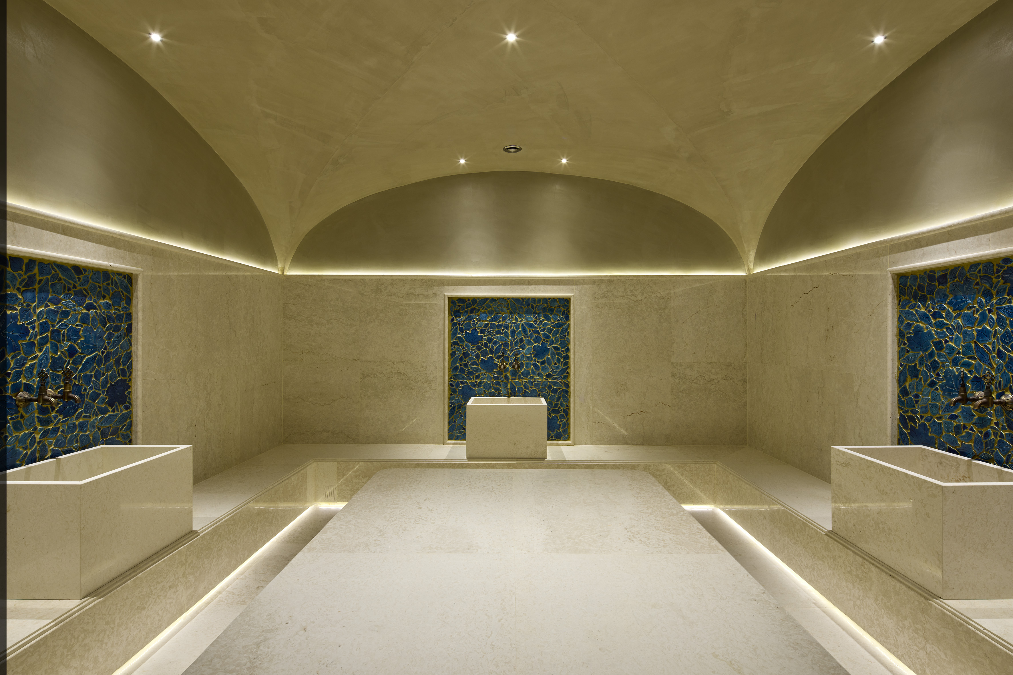 Luxury hammam spa with vaulted ceiling, marble, and blue mosaic walls.