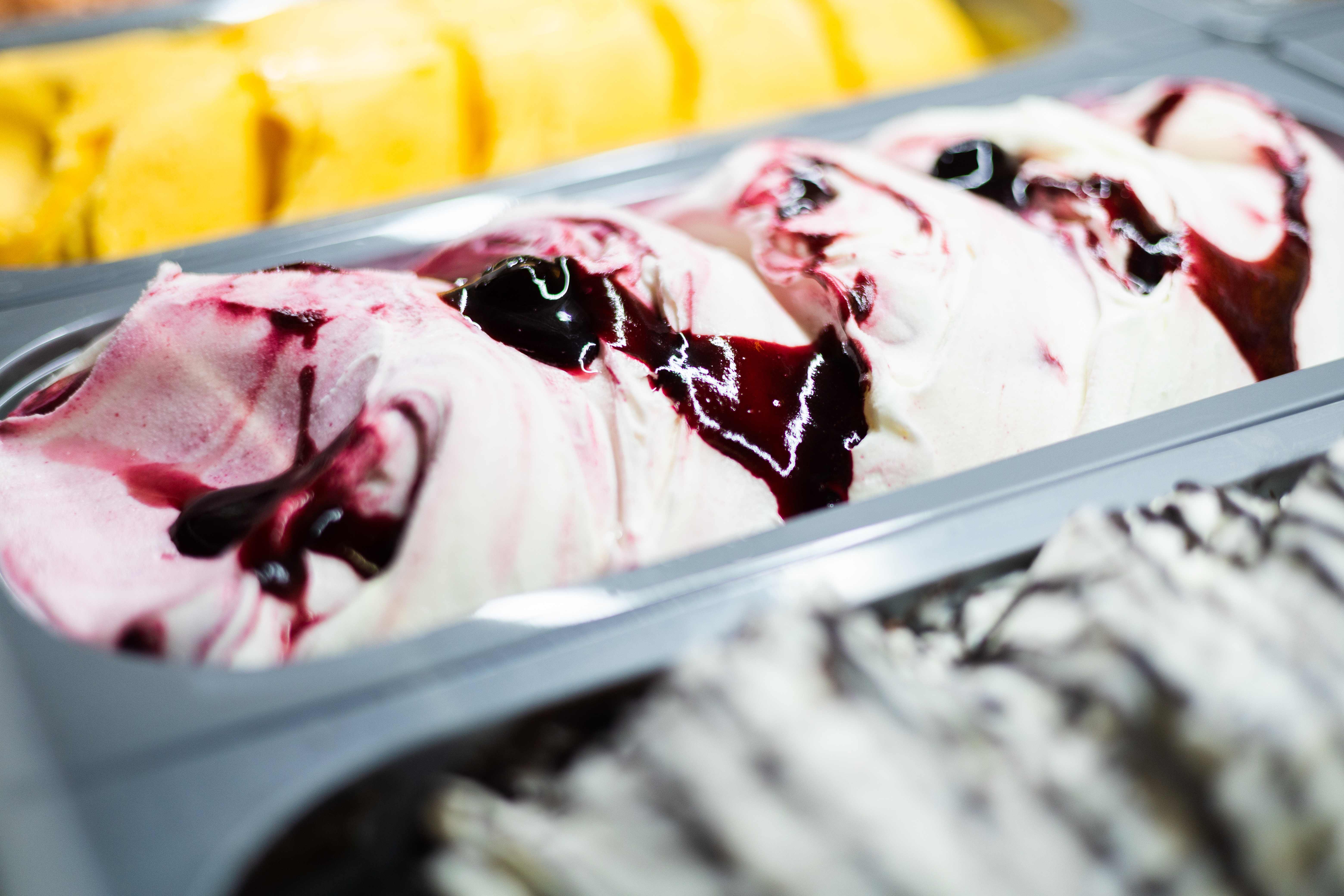 Berry swirl gelato tub in a freezer display, with yellow and striped flavors.