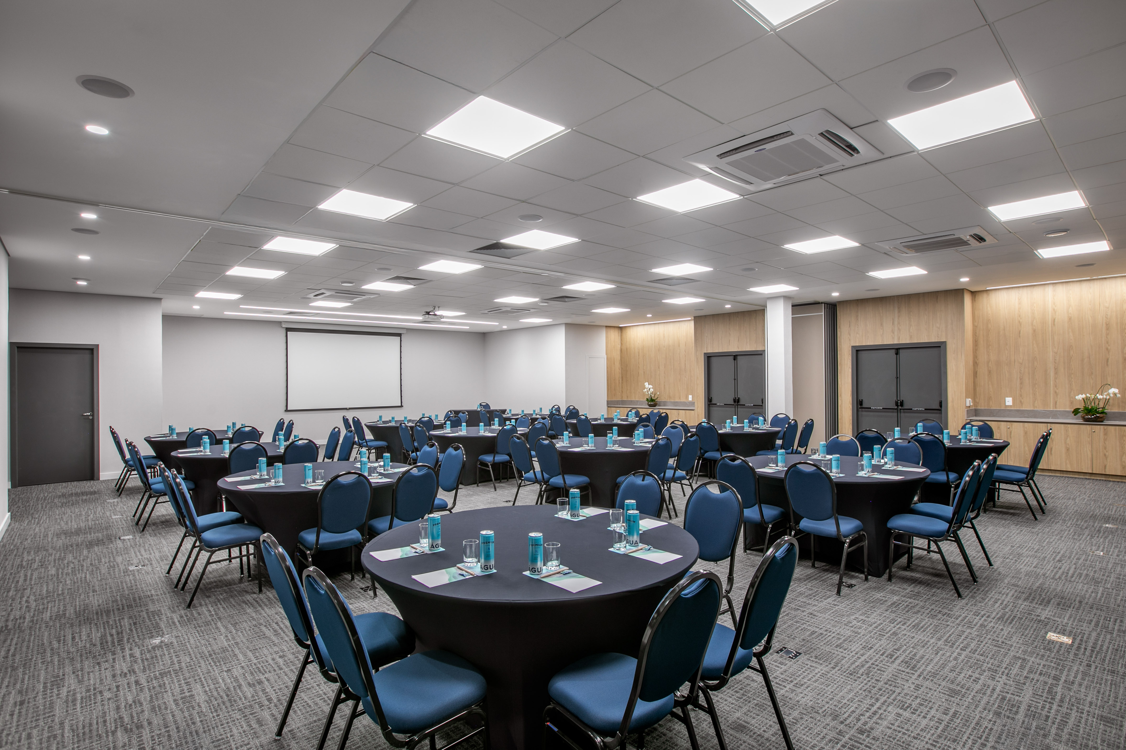 Modern conference room with round tables, blue chairs, and a projector screen.