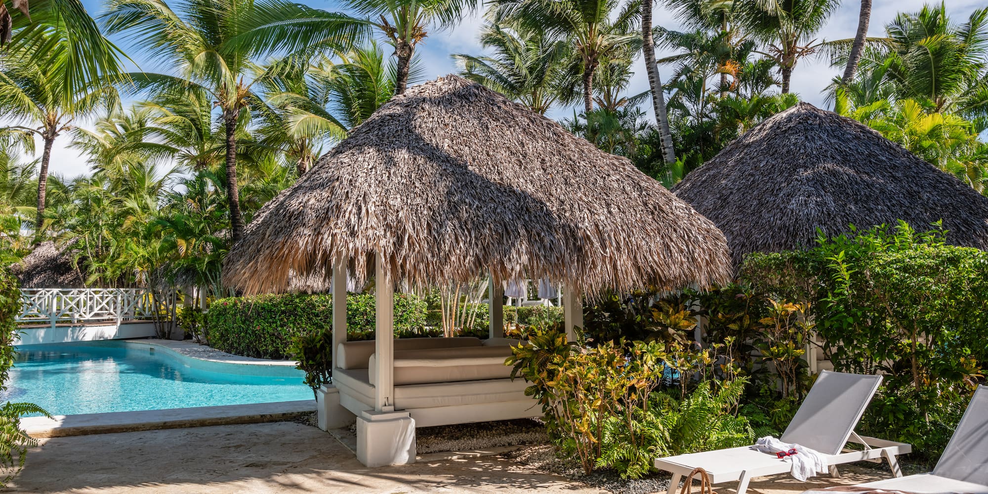 a beach hut with a straw roof and a pool in the background