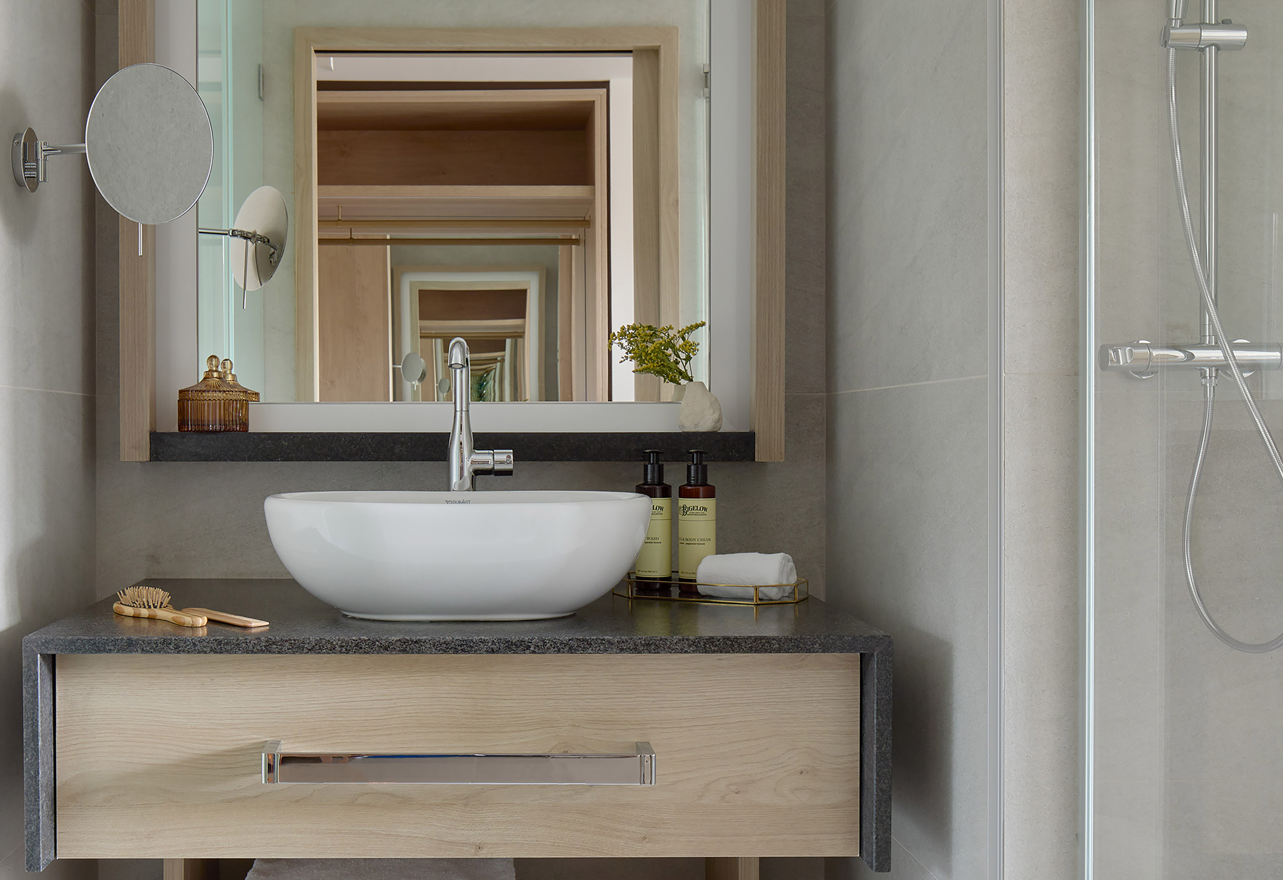 Modern bathroom vanity, white bowl sink, wood cabinet, stone counter, shower.