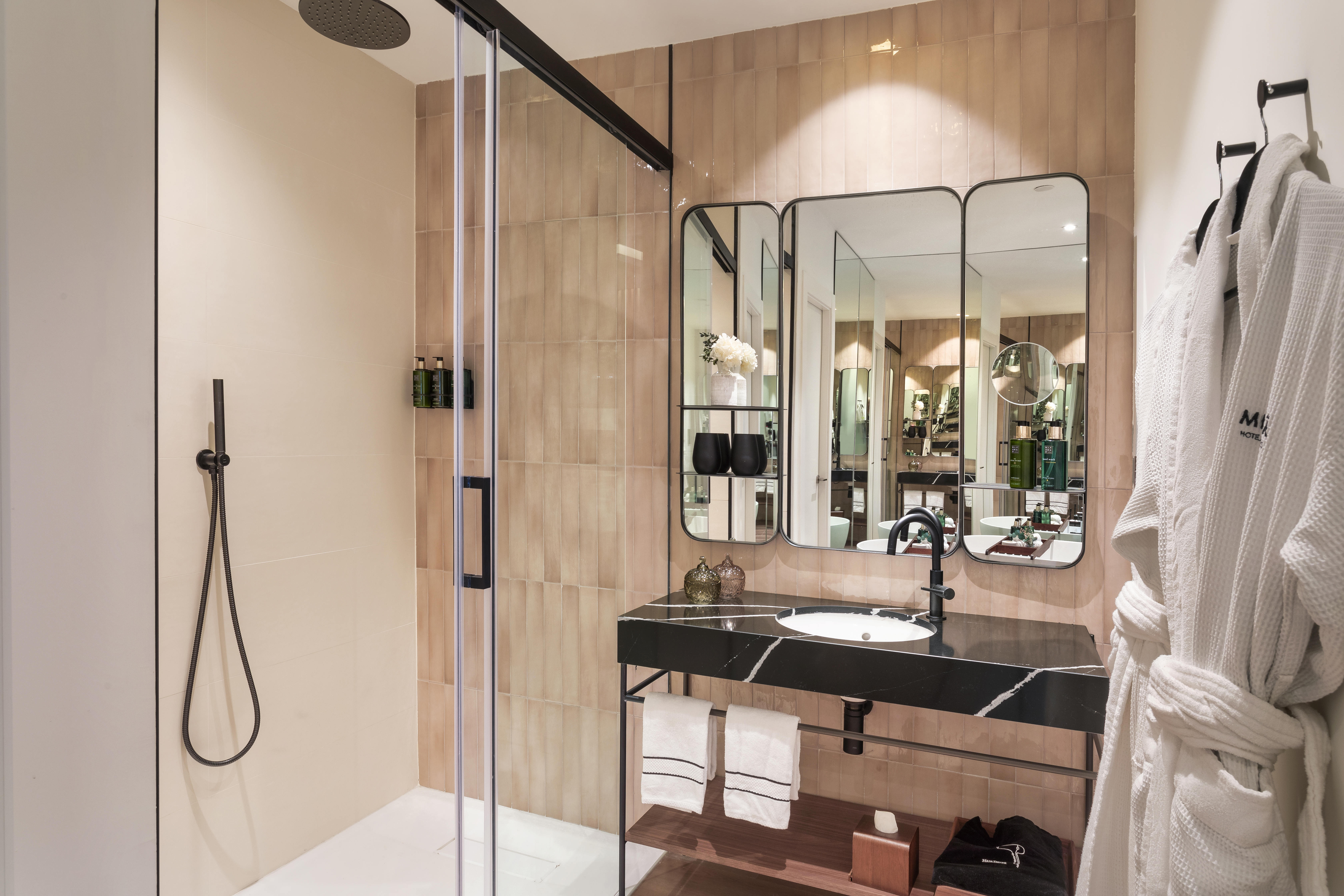 Modern hotel bathroom with glass shower, black marble vanity, and white bathrobes.