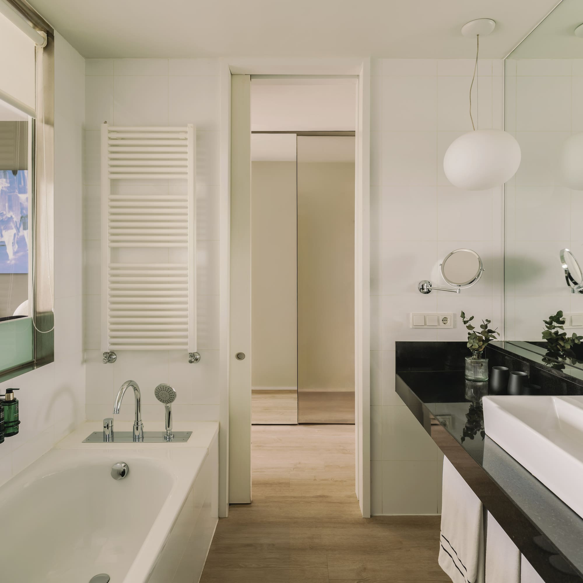 Baño moderno con bañera, lavabo blanco, encimera negra y espejo.