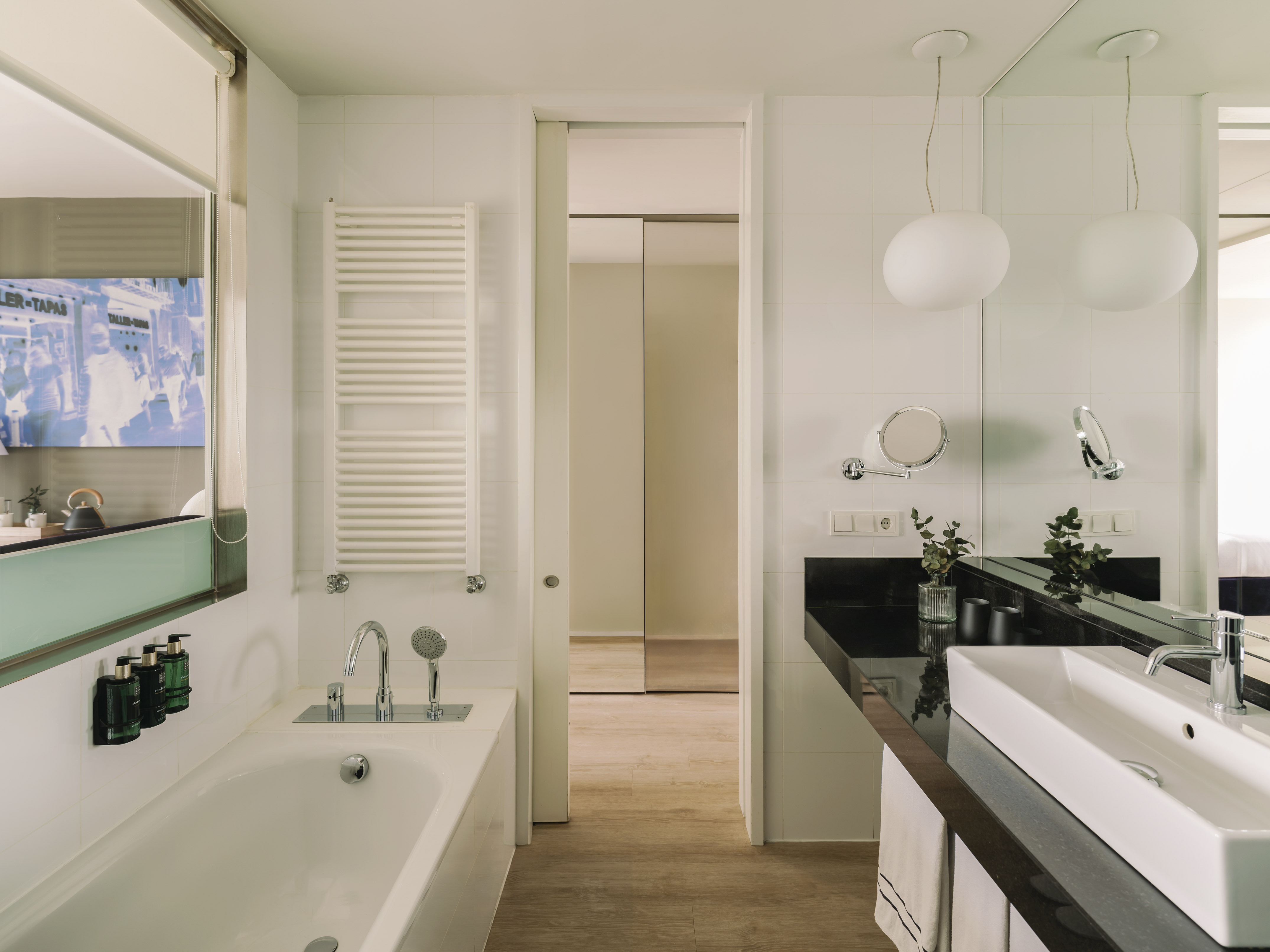 Baño moderno con bañera, lavabo blanco, encimera negra y espejo.