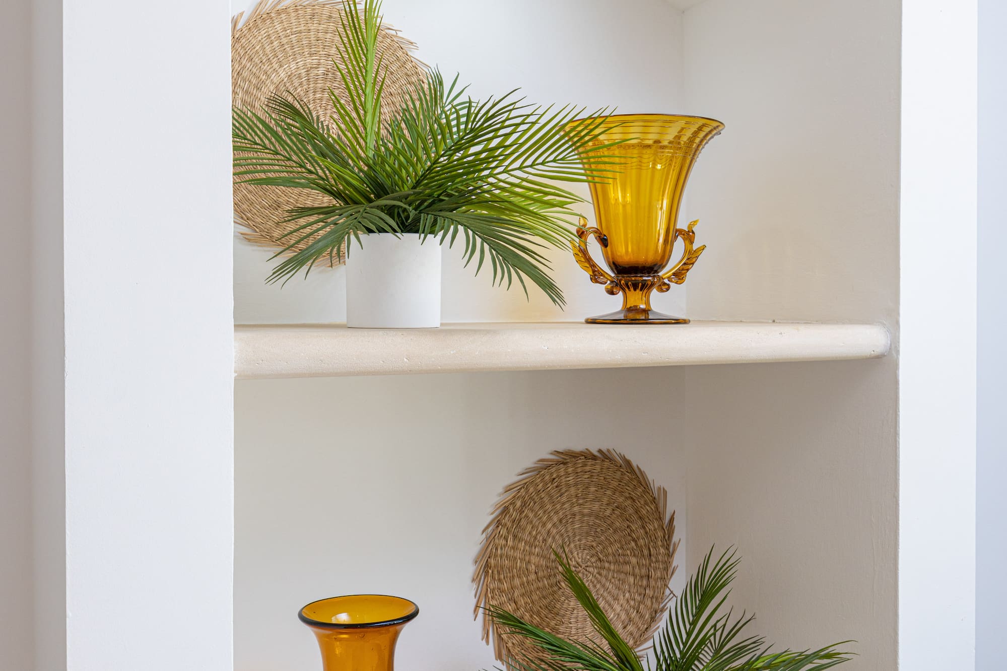 Stylish white built-in niche with amber glass vases, potted palms, and woven accents.