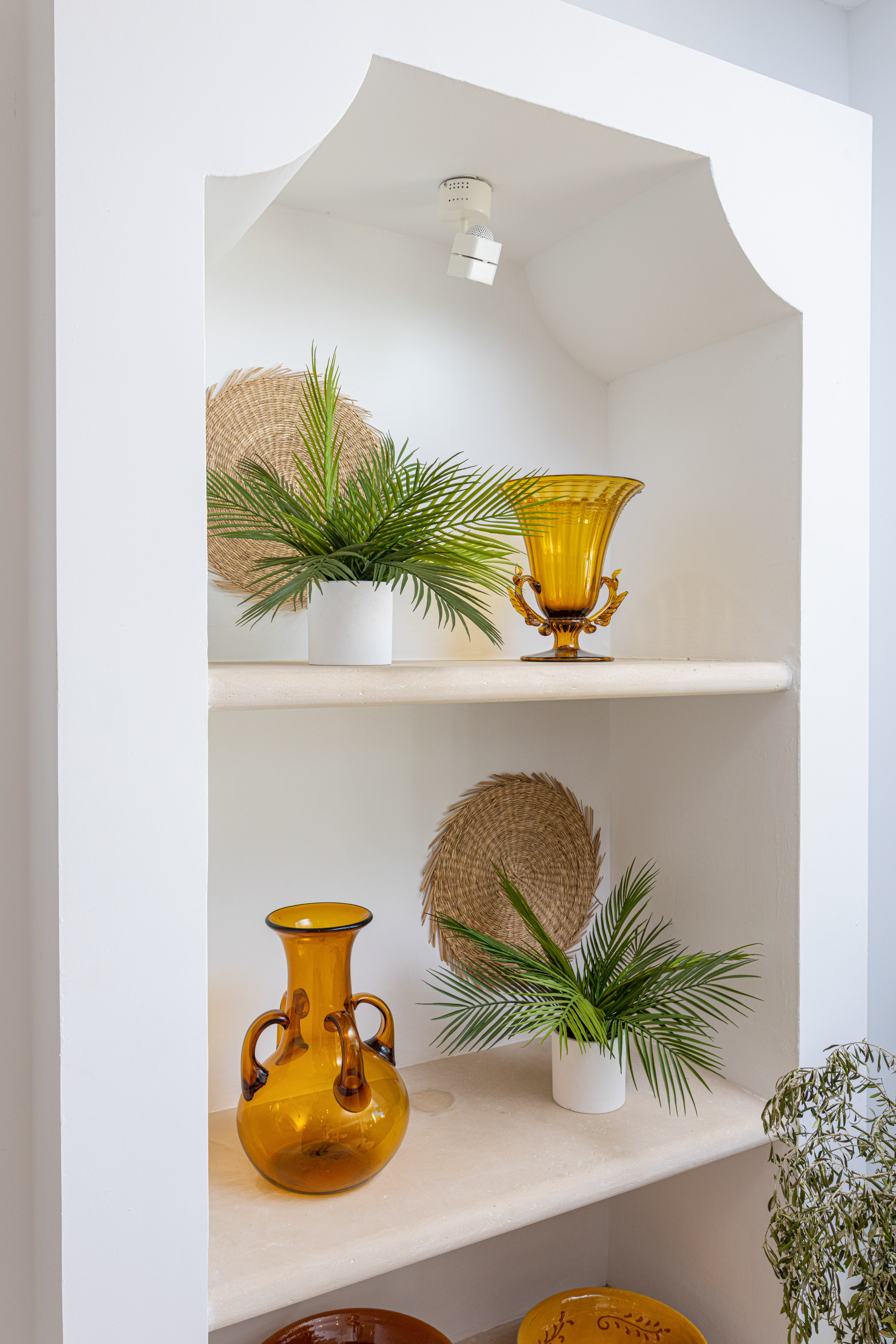 Stylish white built-in niche with amber glass vases, potted palms, and woven accents.