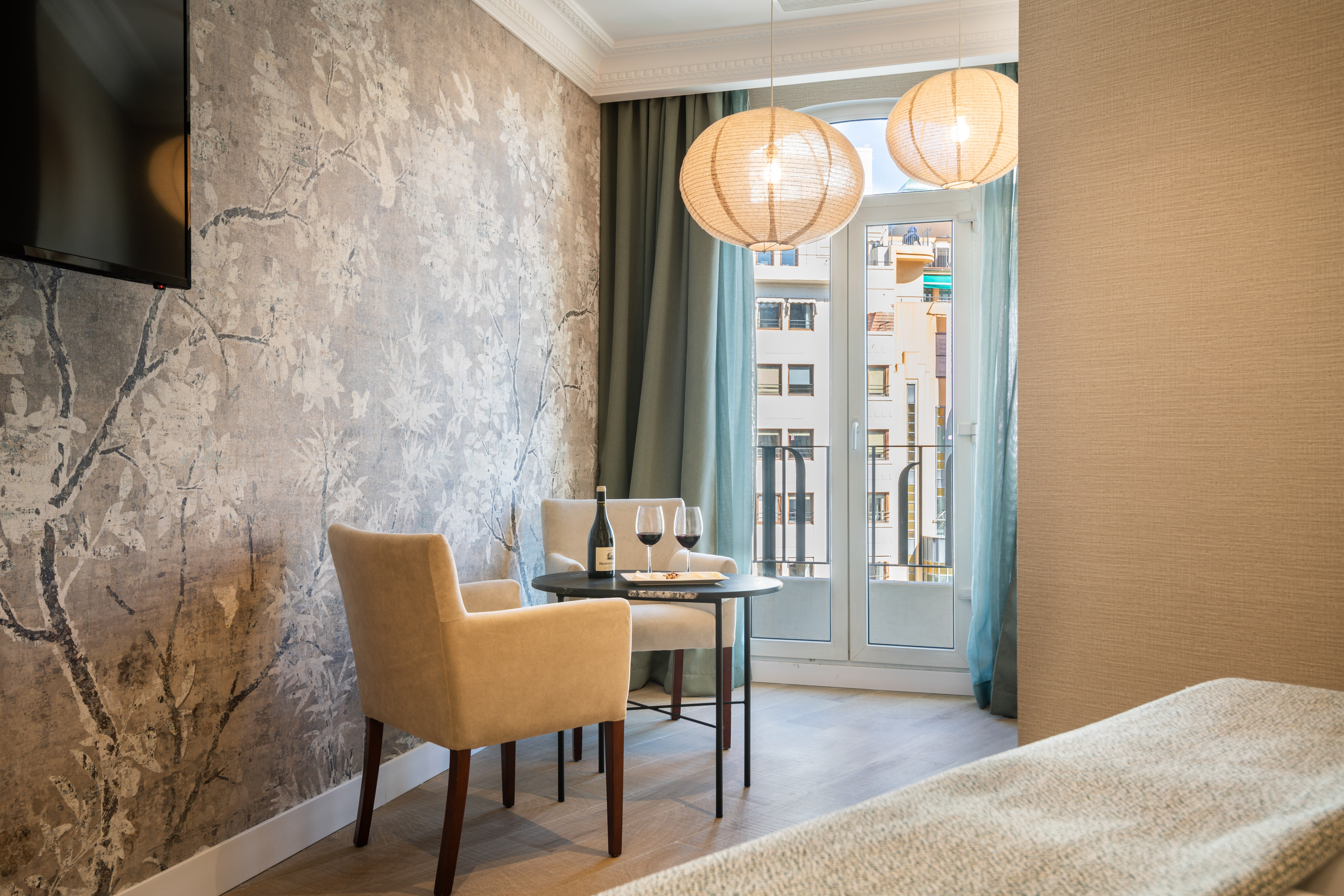 Cozy hotel room with romantic table, wine, floral wallpaper, and city view.