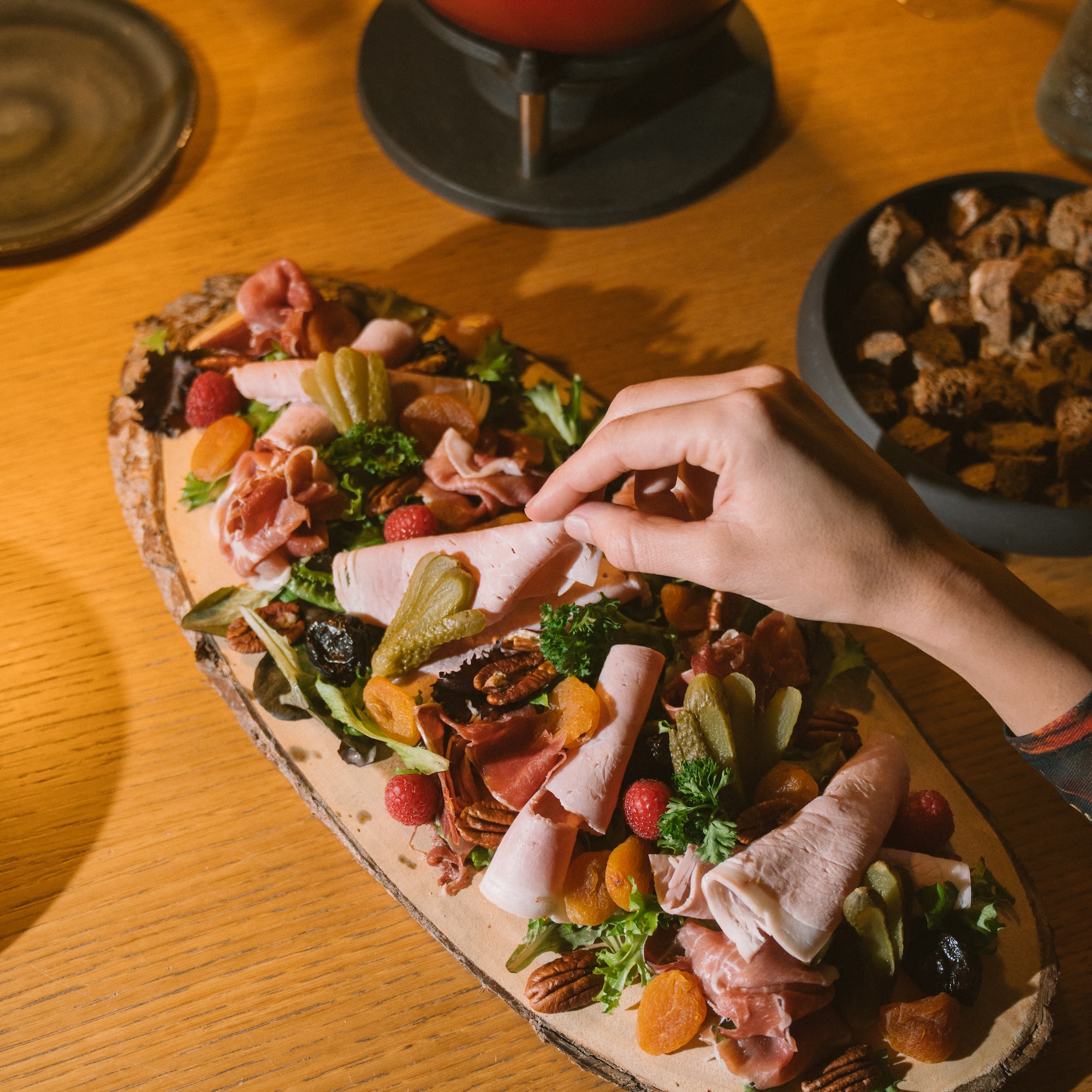 Hand picking ham from charcuterie board, with cheese fondue and wine.