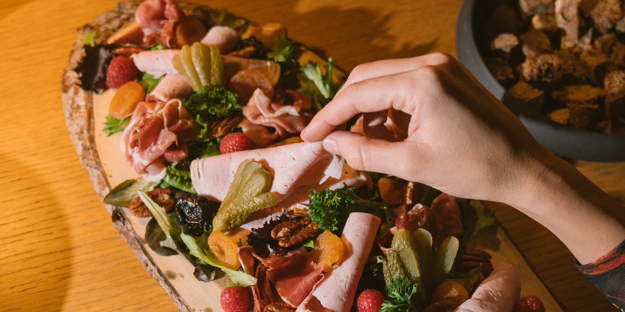 Hand picking ham from charcuterie board, with cheese fondue and wine.