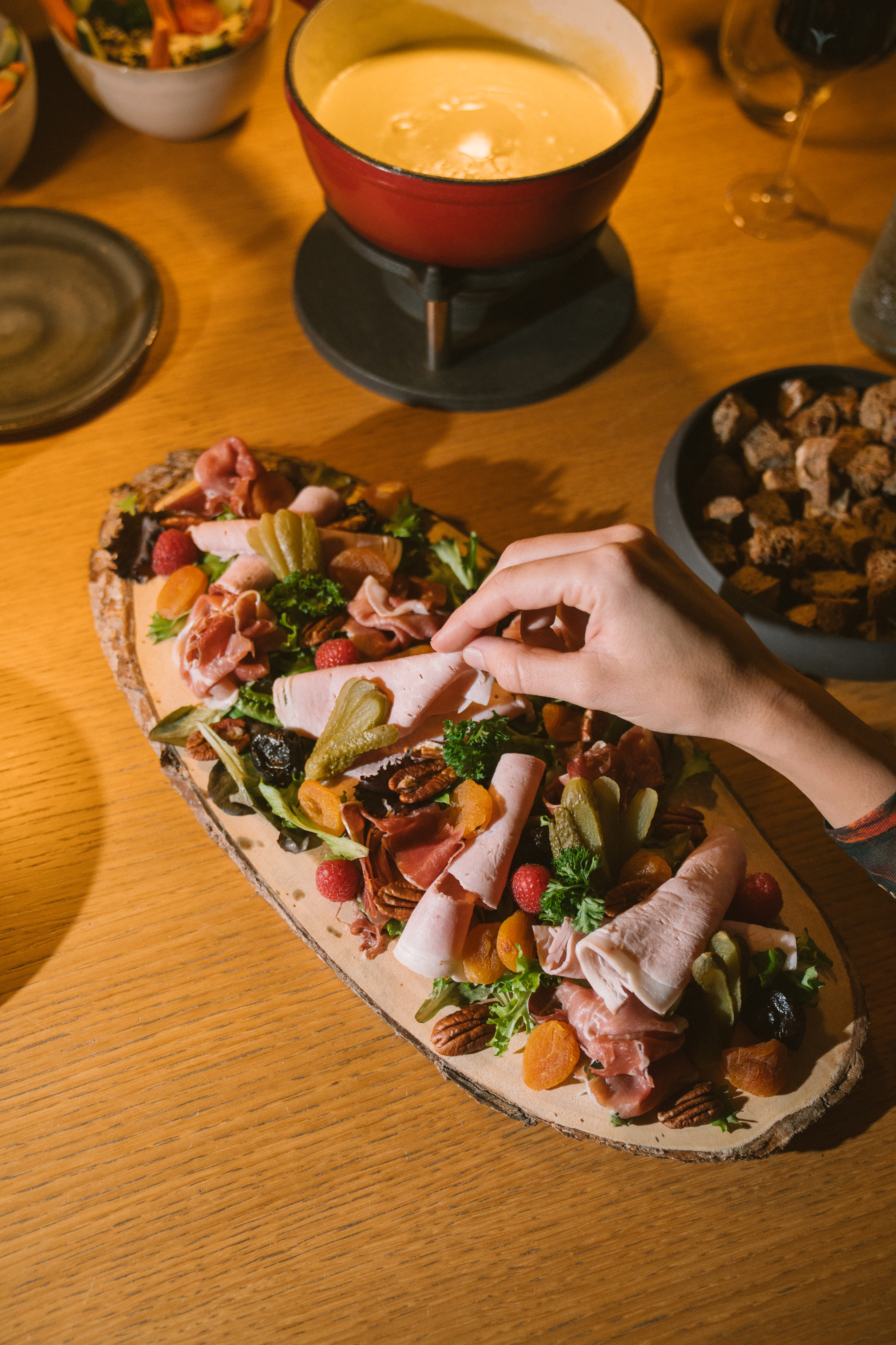 Hand picking ham from charcuterie board, with cheese fondue and wine.