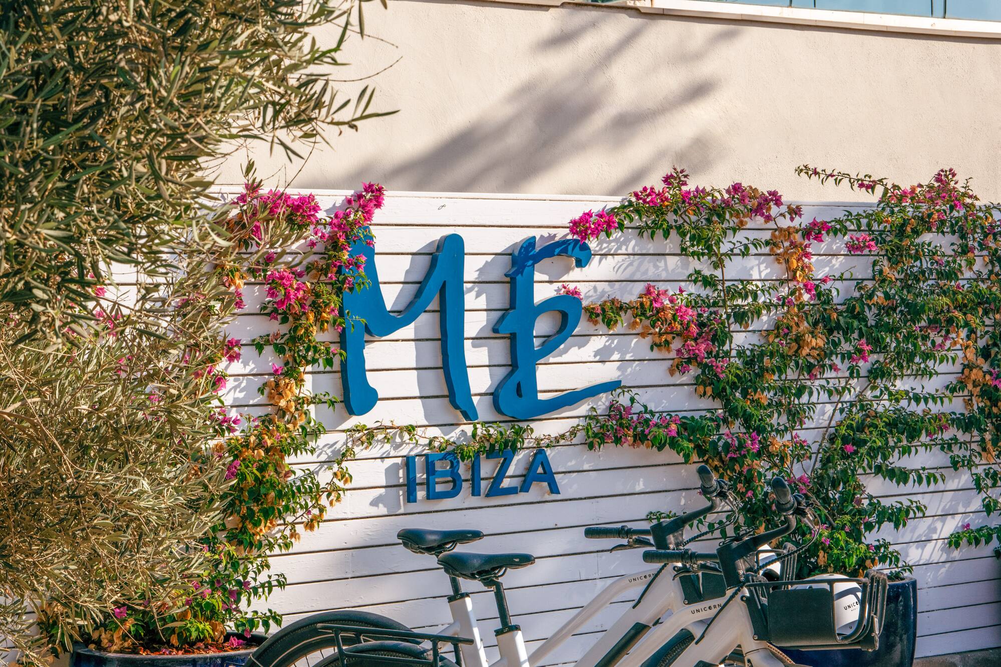 ME Ibiza hotel entrance with two e-bikes and vibrant pink bougainvillea.