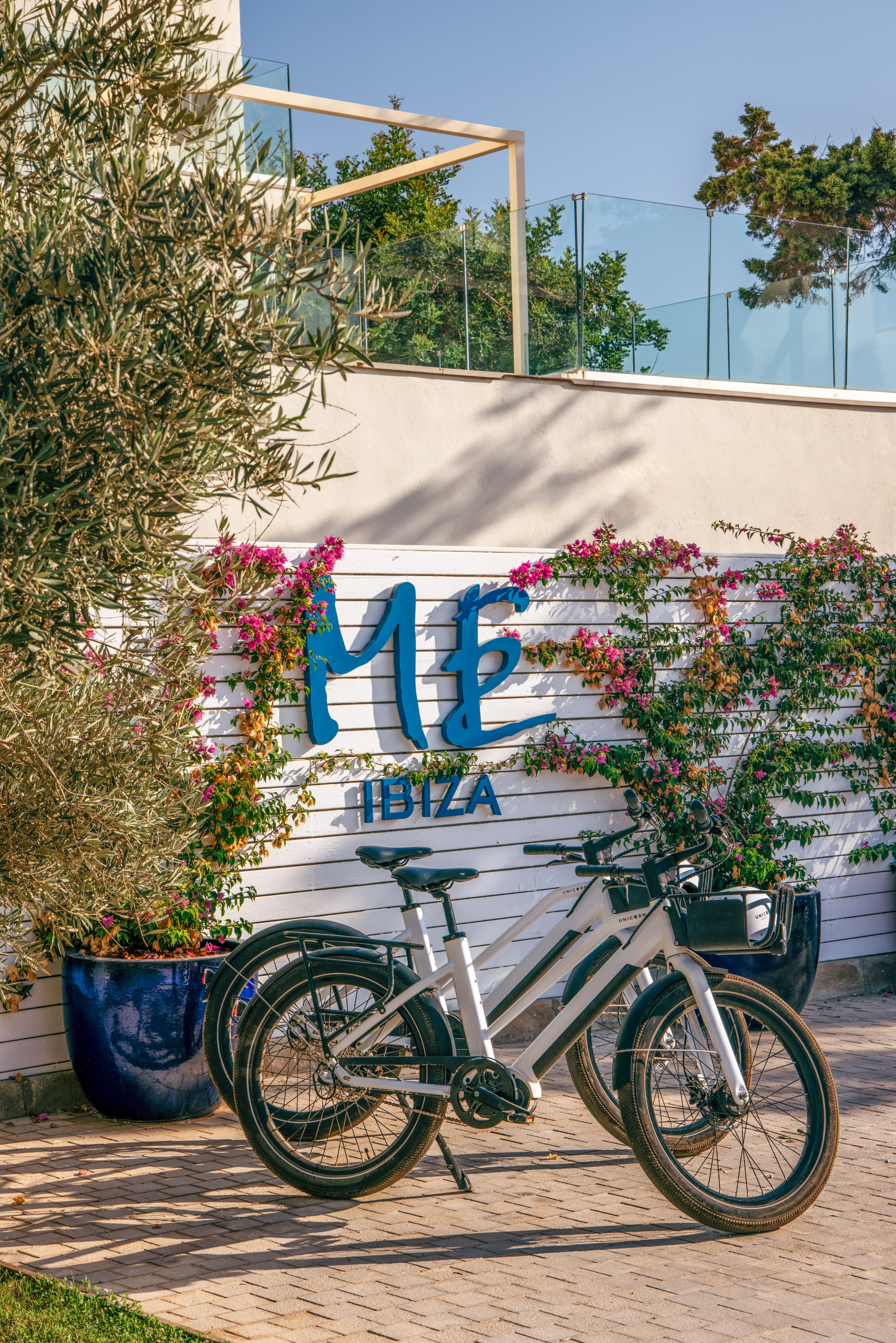 ME Ibiza hotel entrance with two e-bikes and vibrant pink bougainvillea.