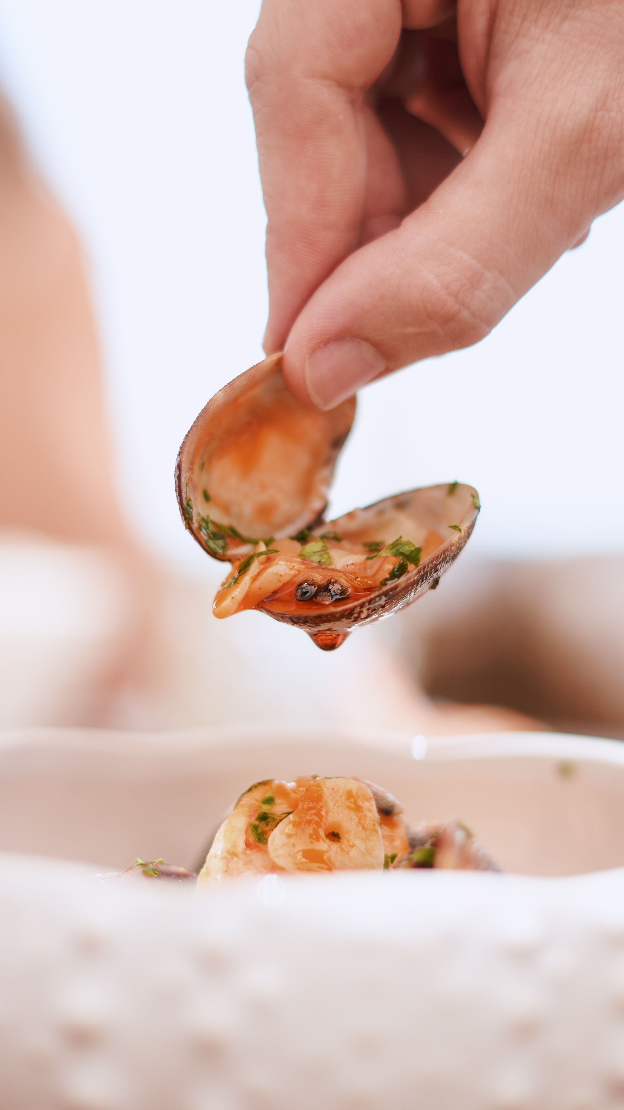 Hand holding seasoned clam with herbs over a seafood dish.