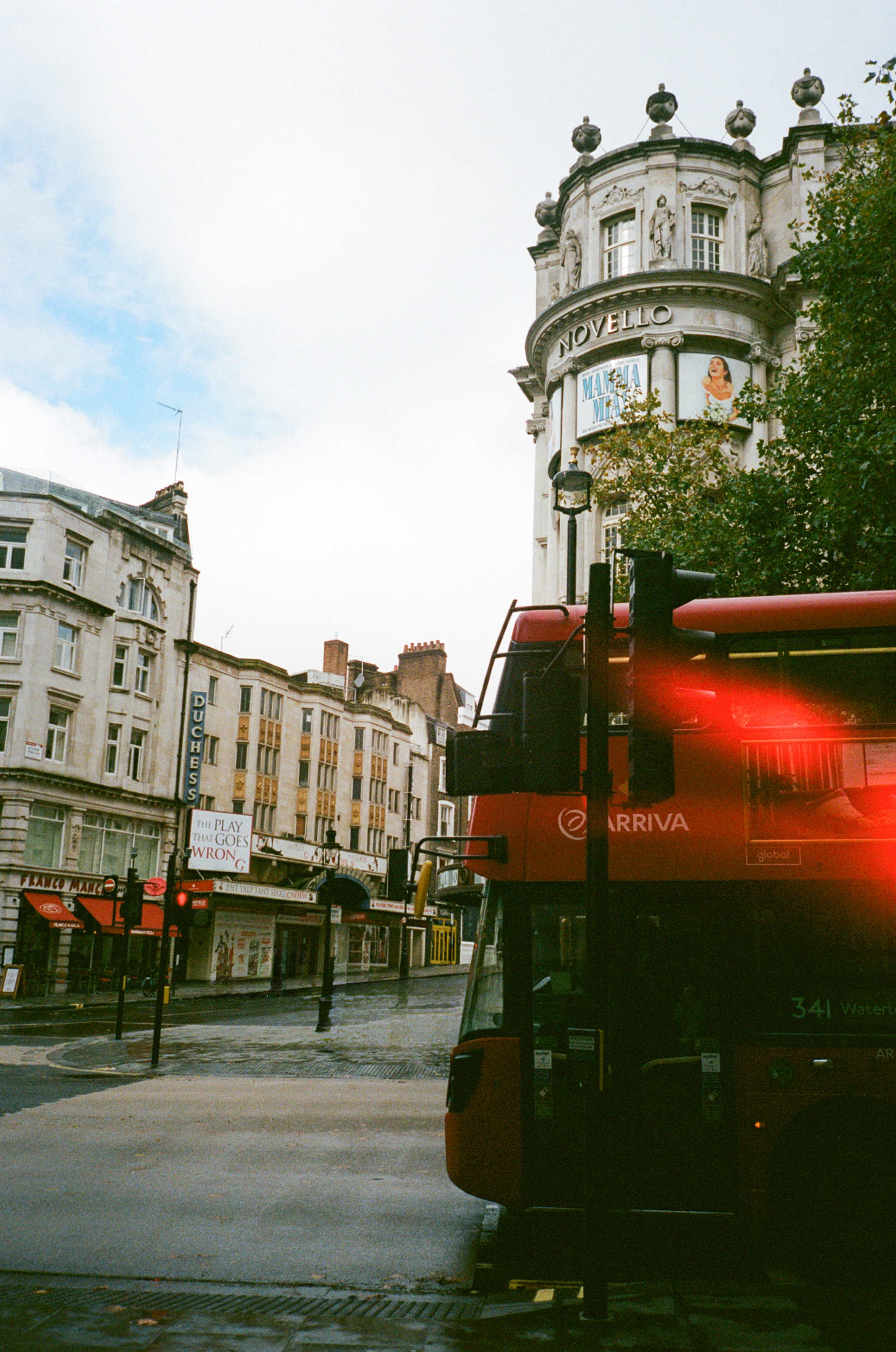 Red London bus on wet city street near Novello and Duchess Theatres.
