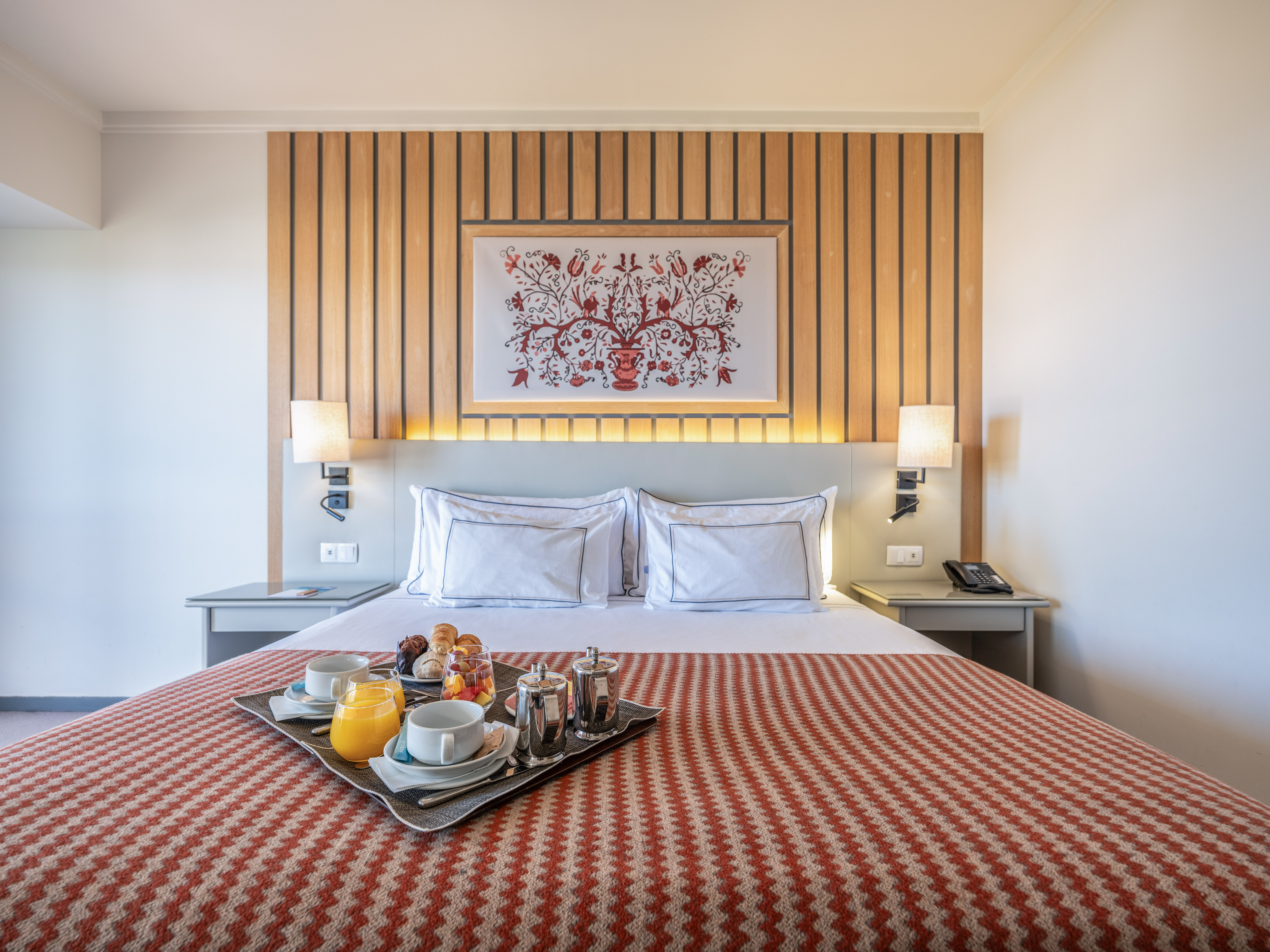 Hotel room with breakfast in bed, wooden headboard, and patterned bedspread.