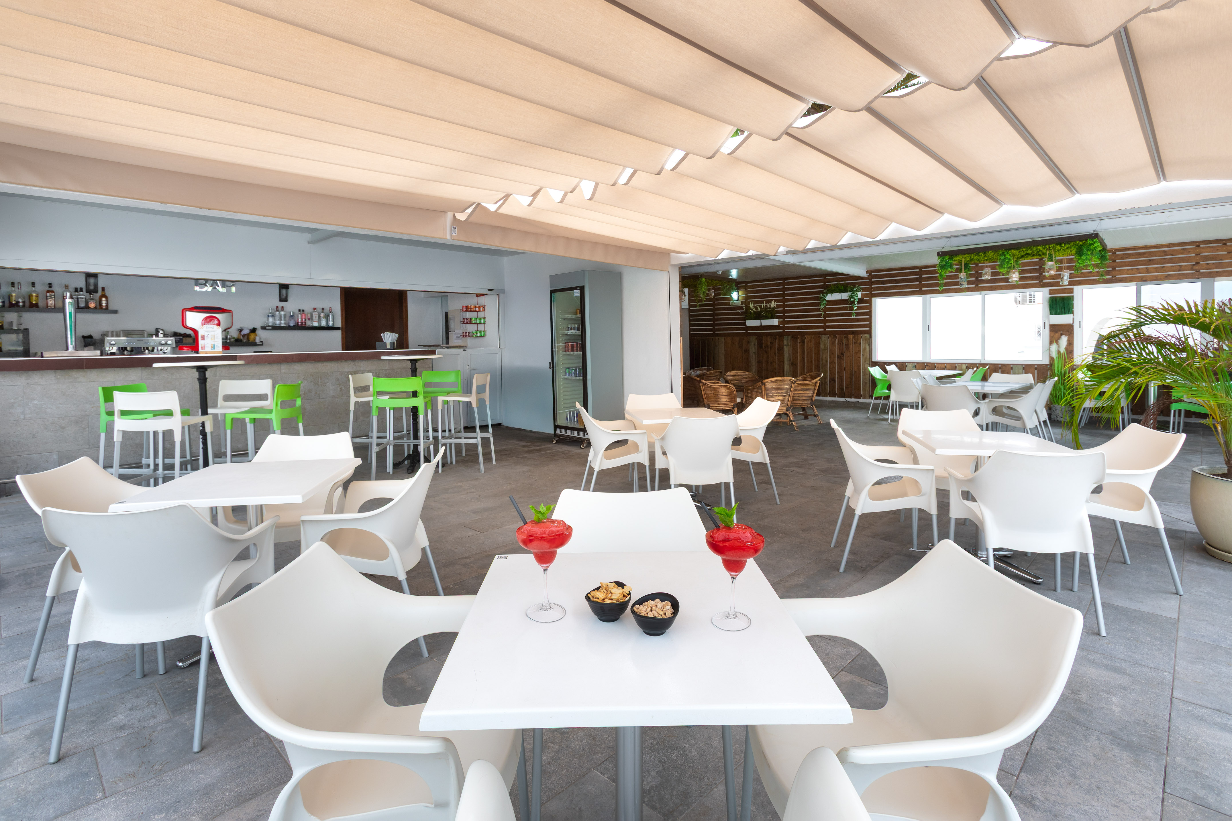 Outdoor bar & restaurant with white seating, retractable canopy, and cocktails.