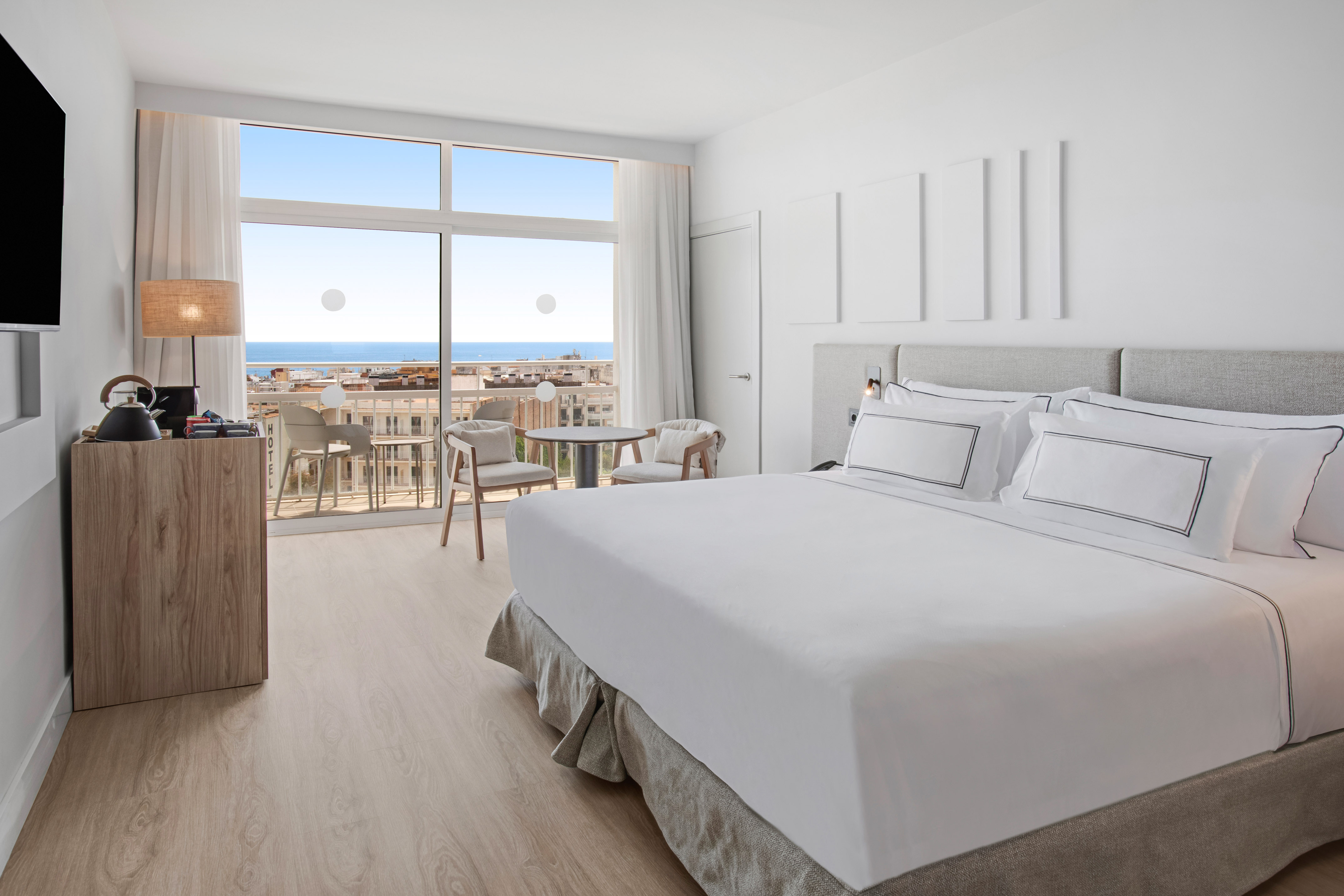 Modern hotel room with ocean view balcony, large bed, and bright decor.