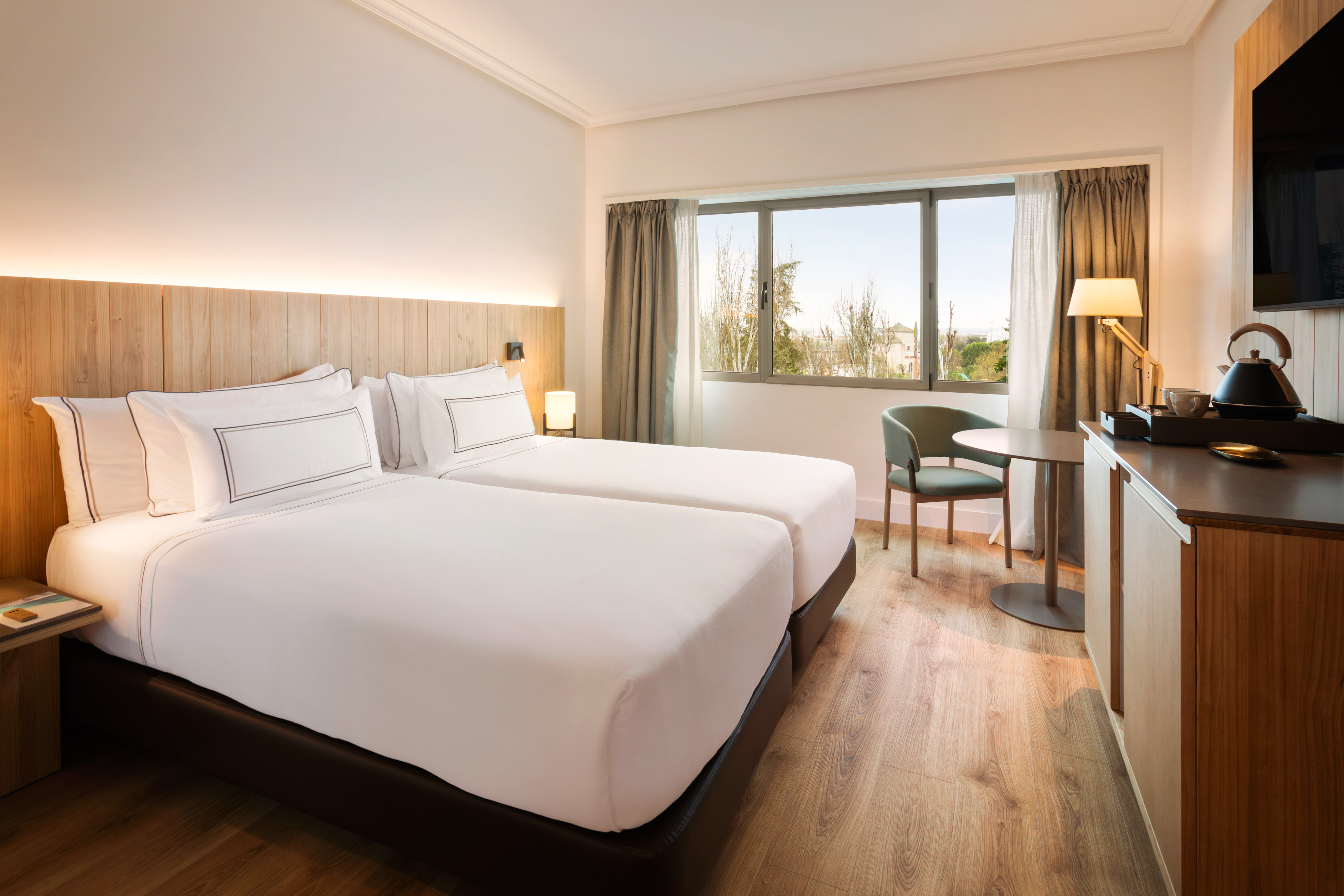 Comfortable hotel room with twin beds, wooden decor, and large window view.
