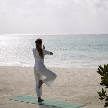 a woman standing on a yoga mat on a beach