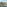 Balcony view of coastal resort with swimming pool, buildings, palm trees, and blue sea.